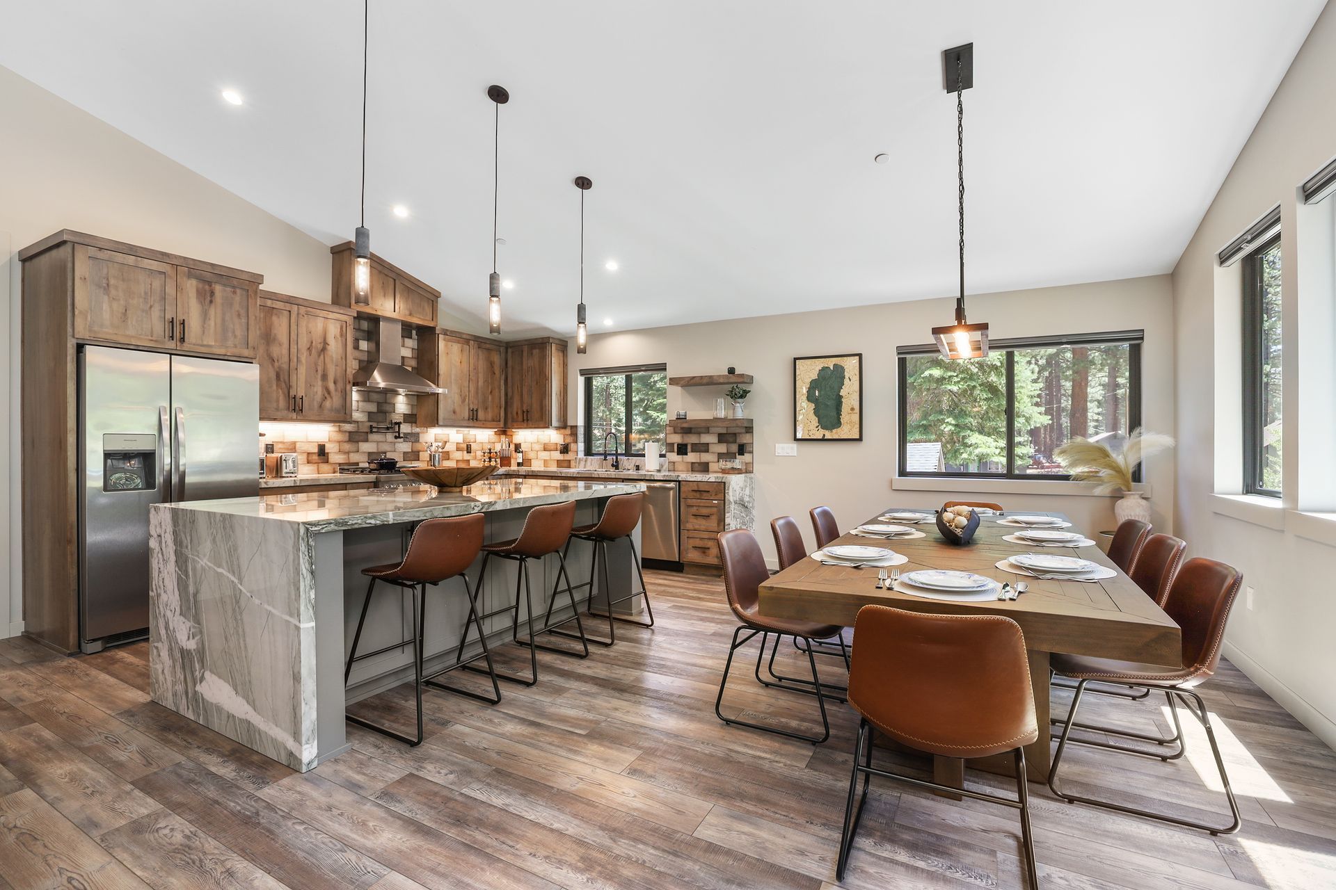 Modern open-concept kitchen and dining area with wood floors, granite island, and brown chairs