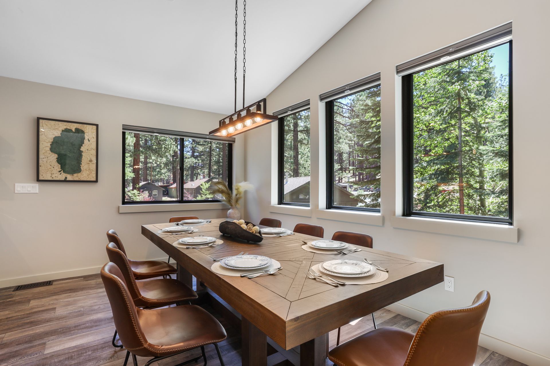 Modern dining room with large windows, wooden table set for a meal, and forest view outside