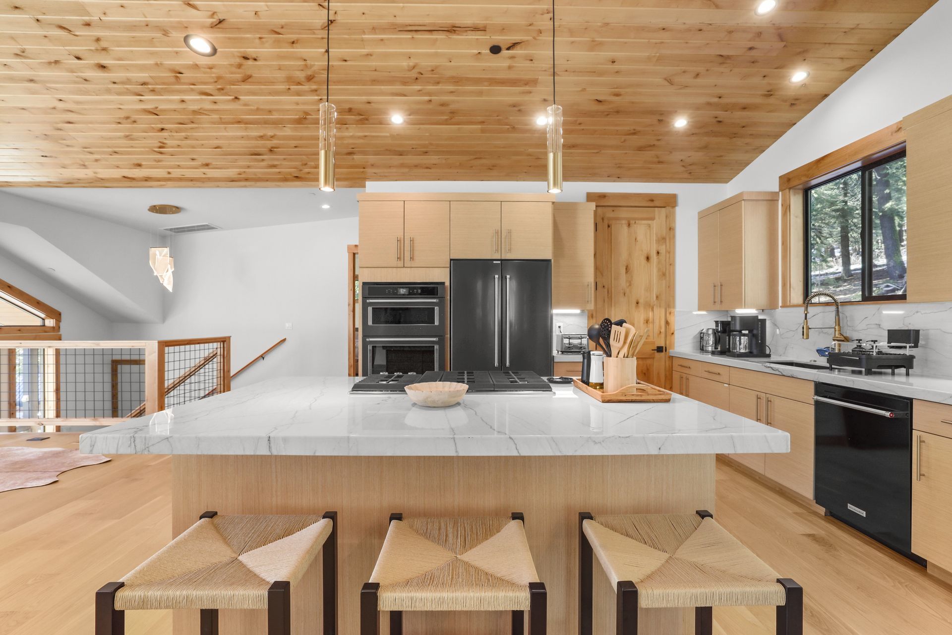 Modern kitchen with a large white island, wood ceiling, black appliances, and three stools