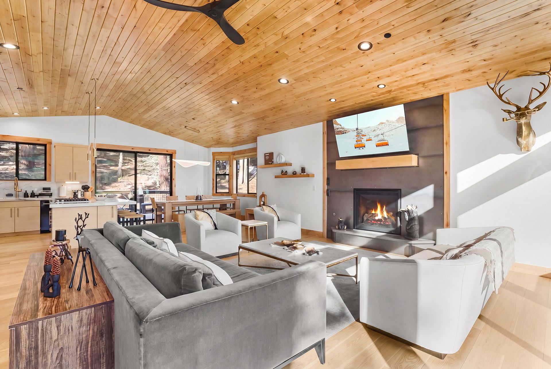 Spacious modern living room with a fireplace, gray sofas, wood ceiling, and mountain views through large windows