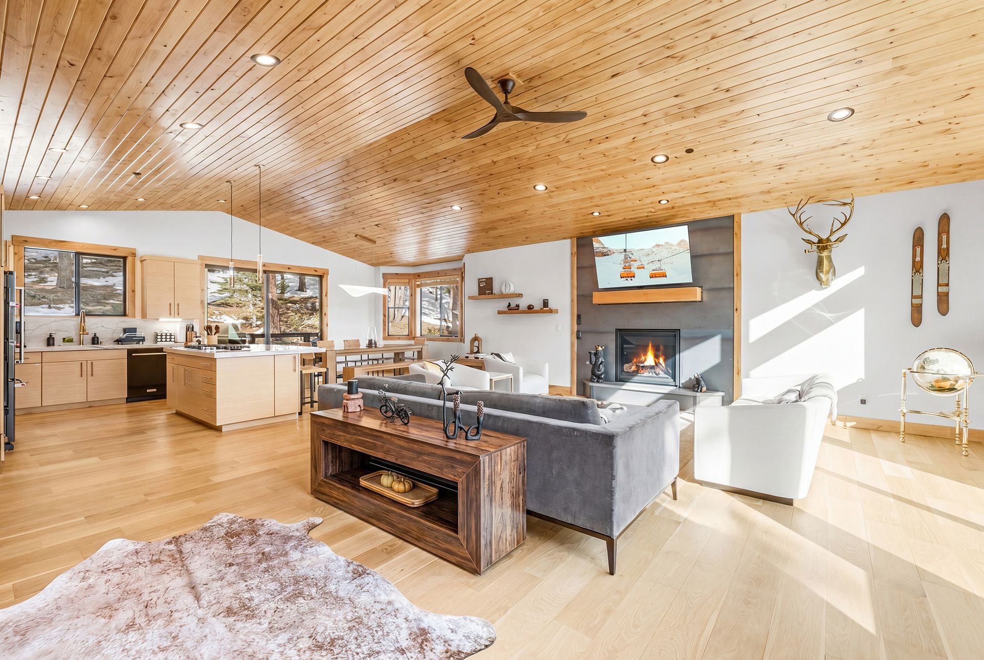 Bright open living room with wood ceiling, central fireplace, and modern kitchen in the background