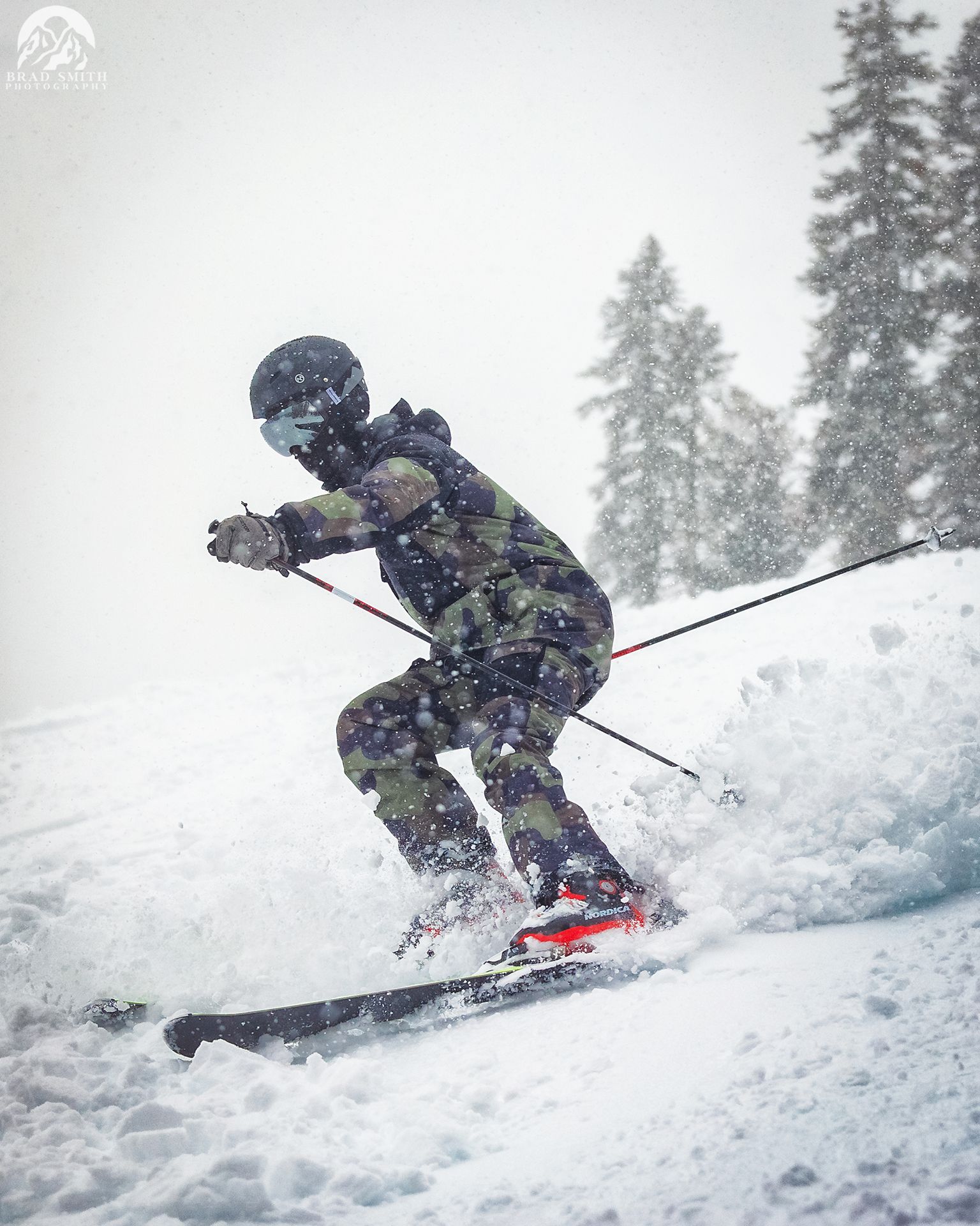 Skier in dark gear carving through deep snow on a snowy mountain slope, with trees in the background