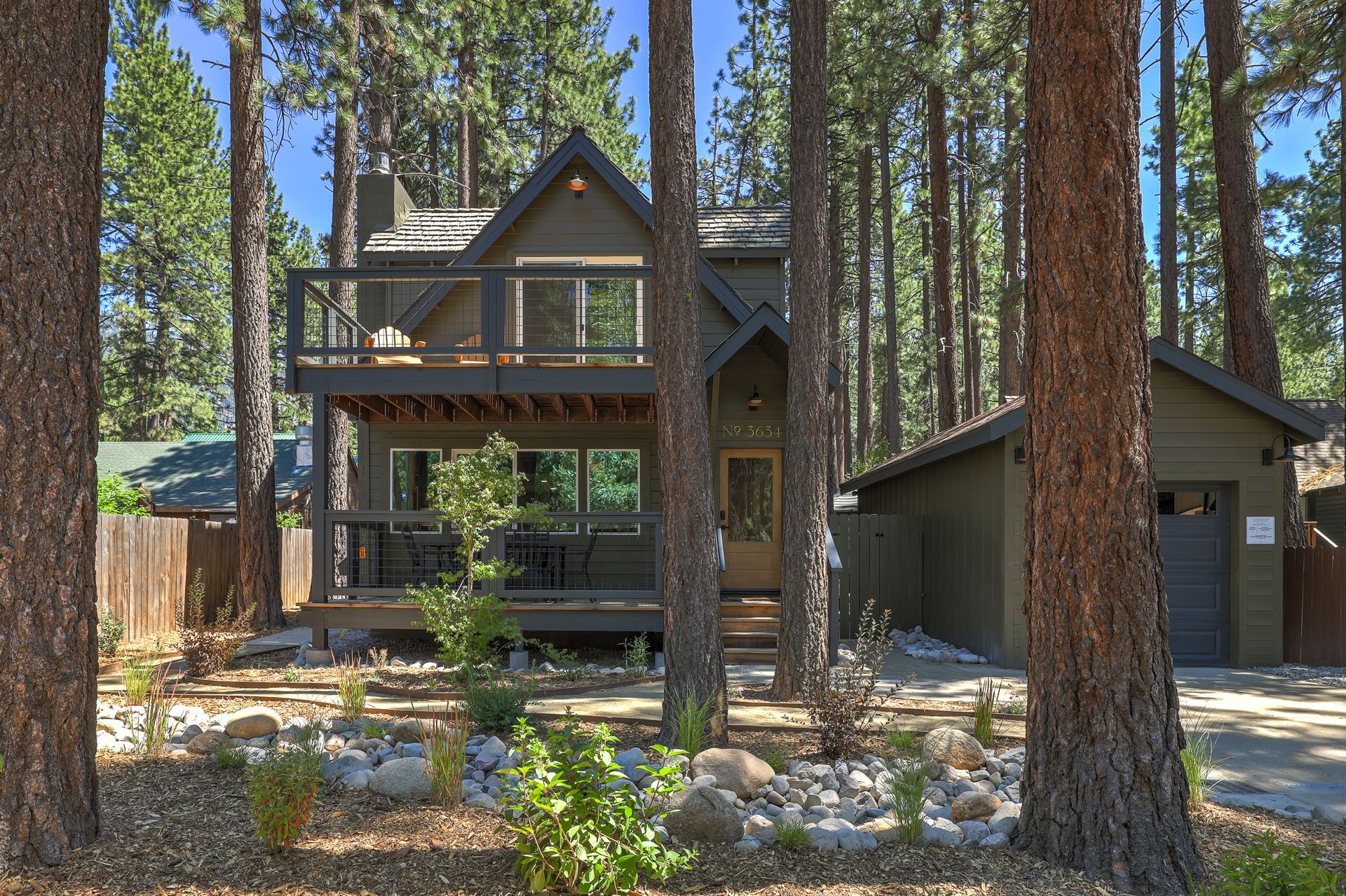 Two-story cabin with a garage among tall pine trees in a wooded setting