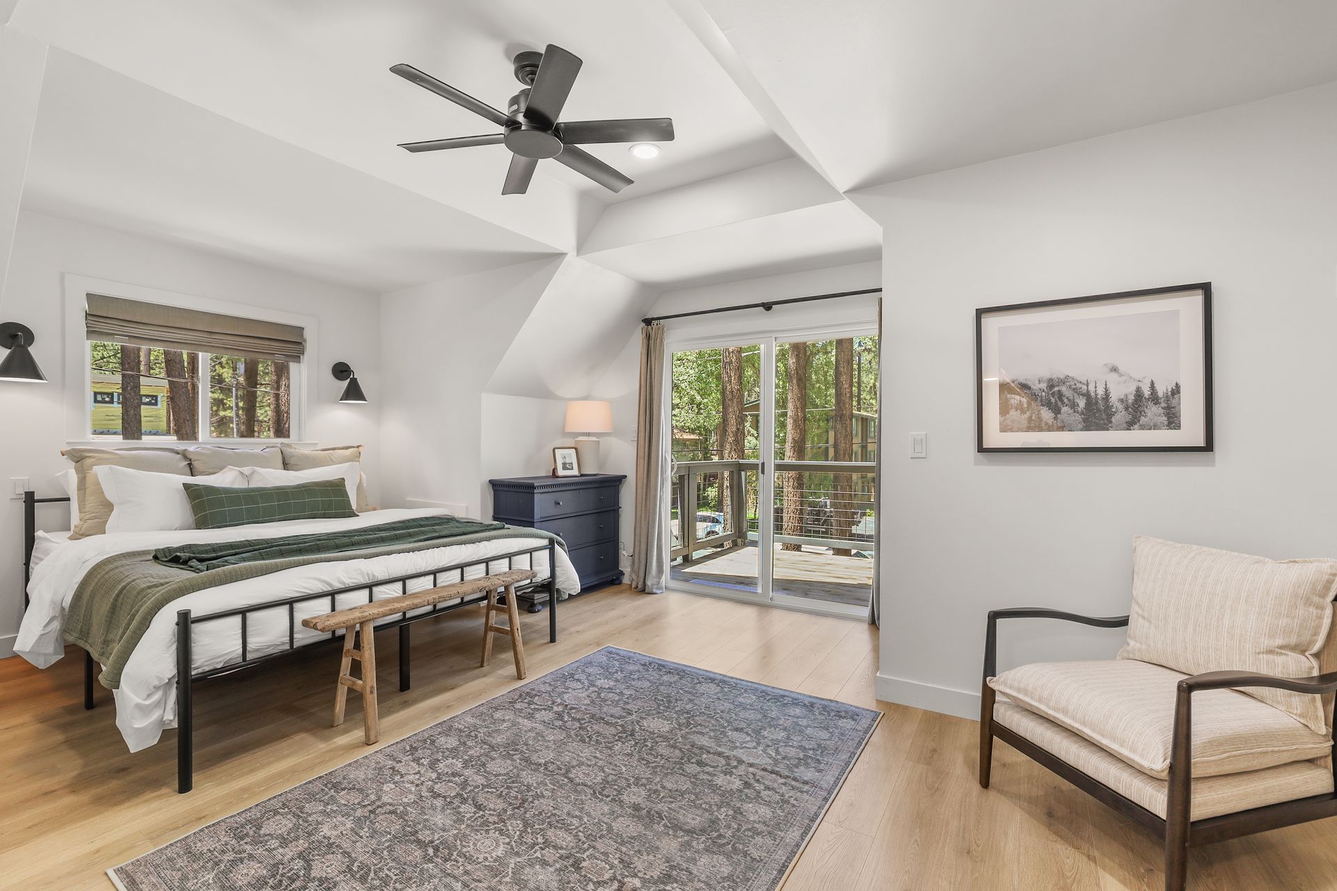Bright bedroom with a bed, bench, chair, rug, and sliding doors to a balcony.