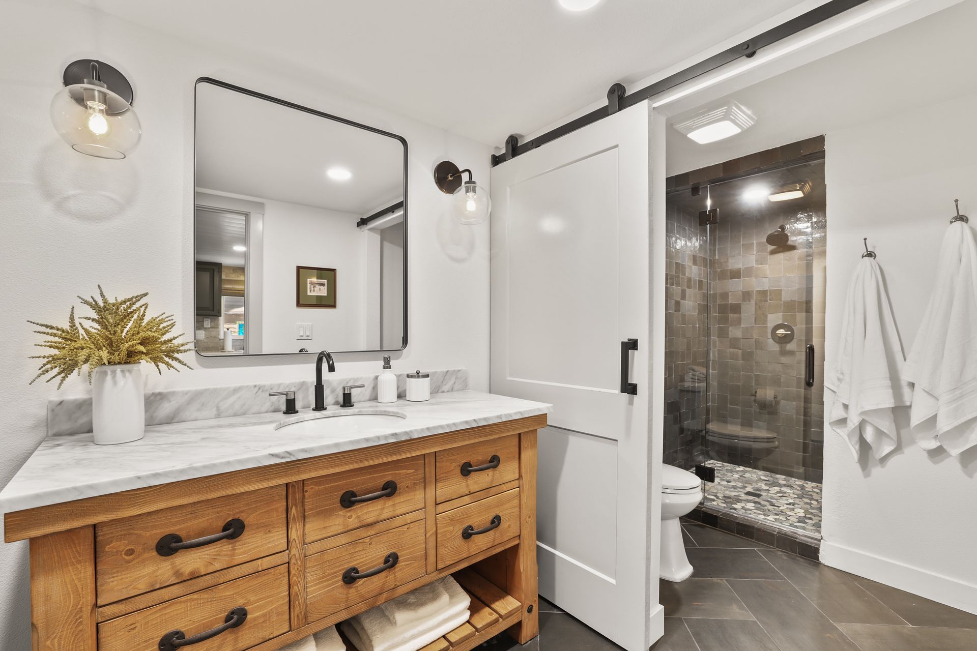 Modern bathroom with wood vanity, large mirror, and open glass shower door