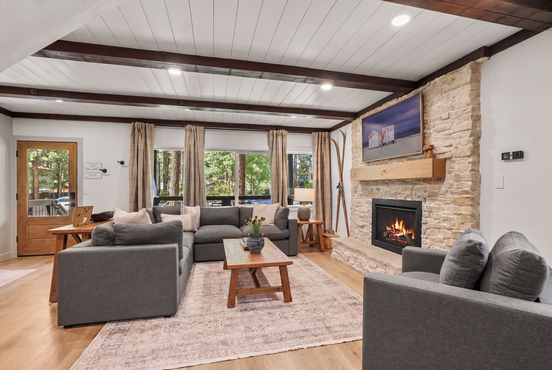 Modern living room with gray sofas, stone fireplace, wood beams, and large windows