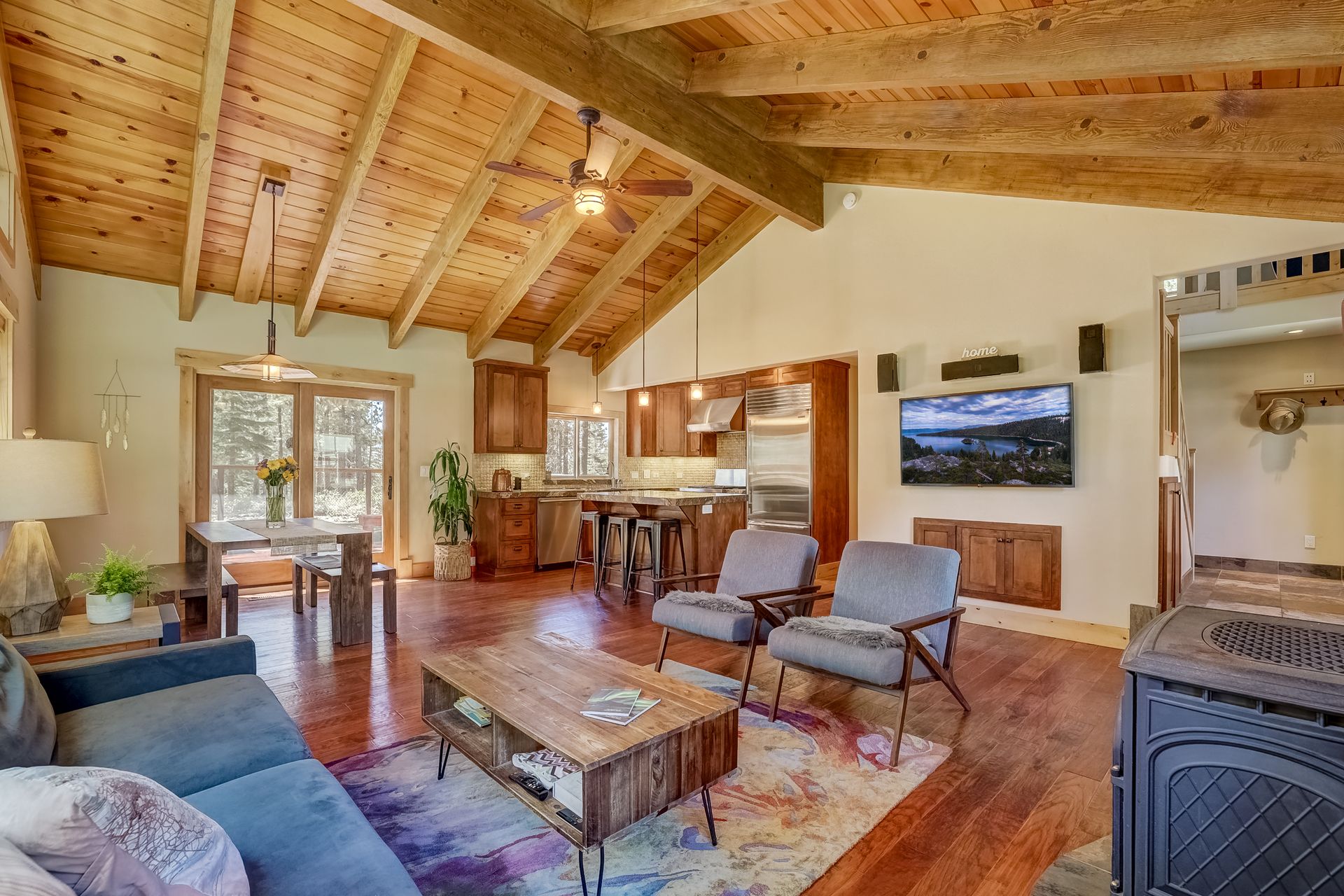 Warm rustic living room with wood beams, stone fireplace, TV, and cozy seating near a large window