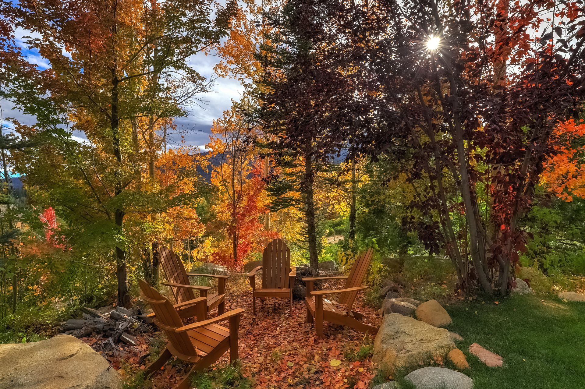 Wooden chairs around a fire pit in a colorful autumn garden with trees and rocks