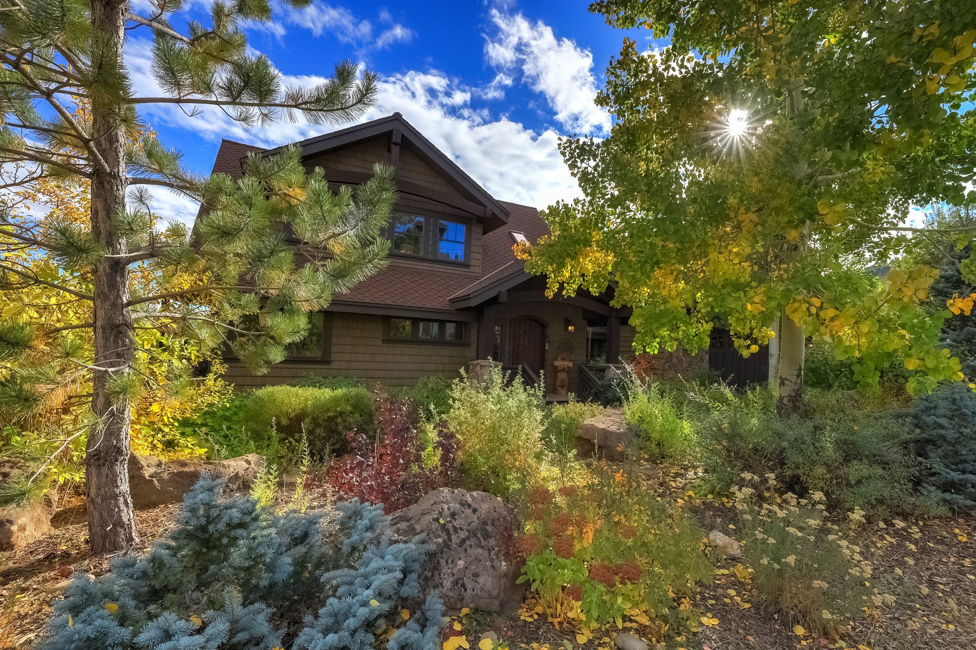 Wooden cabin nestled among autumn trees and shrubs under a bright blue sky