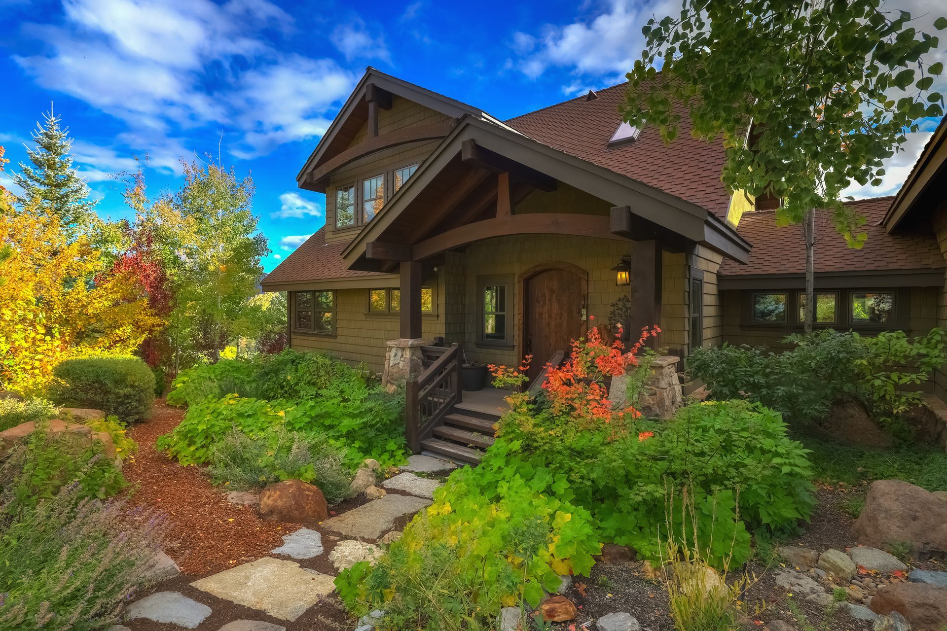 Cozy house with a front porch, stone path, and lush autumn garden under a blue sky