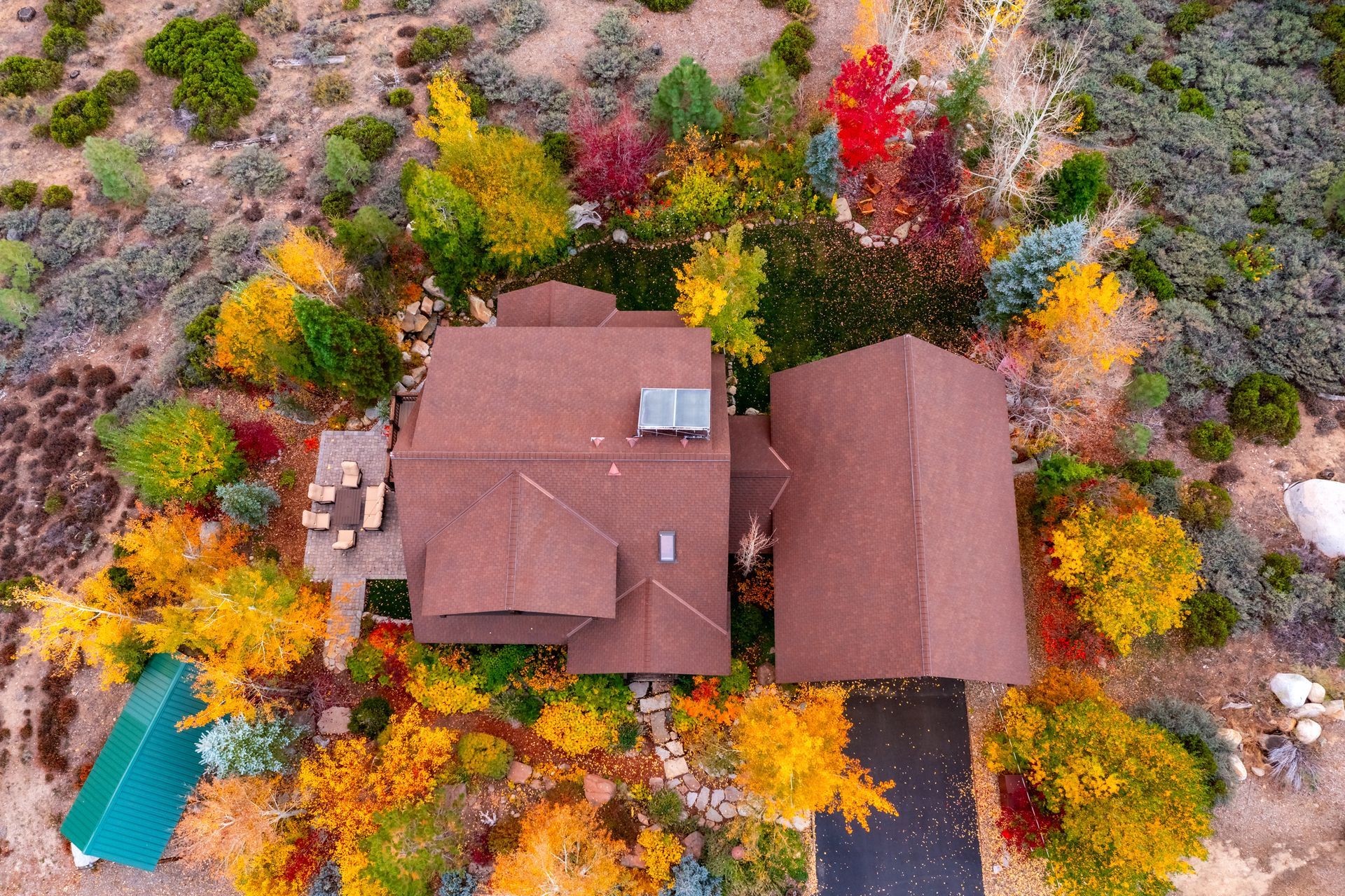 Aerial view of a house with autumn-colored trees and a driveway in a rural landscape