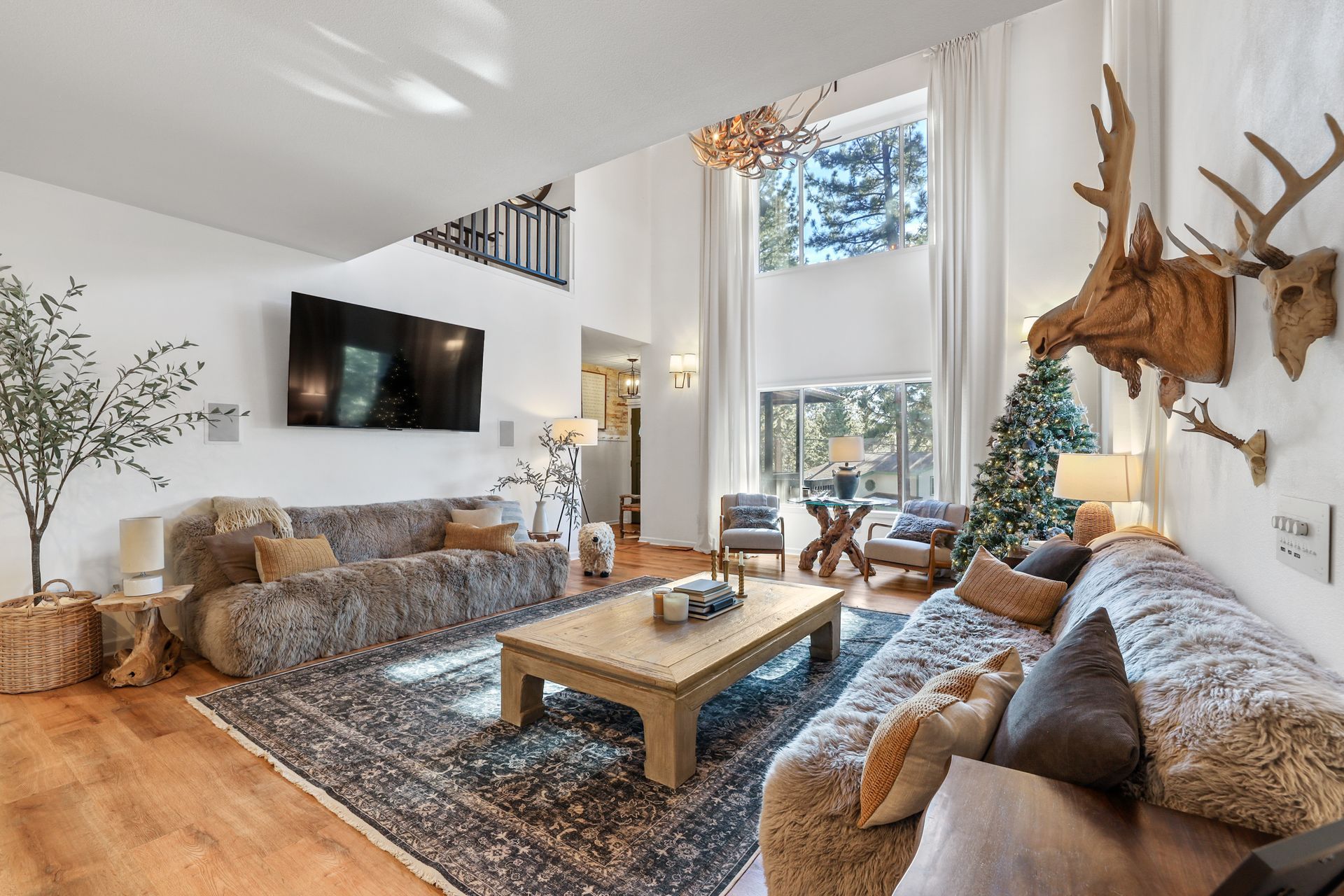 Bright living room with vaulted ceiling, wall-mounted TV, sectional sofa, coffee table, and deer mount decor.