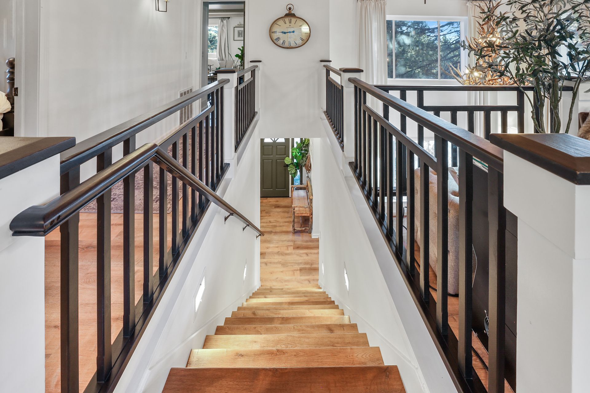 Modern staircase with wooden steps, black railings, and a clock hanging on the wall at the landing