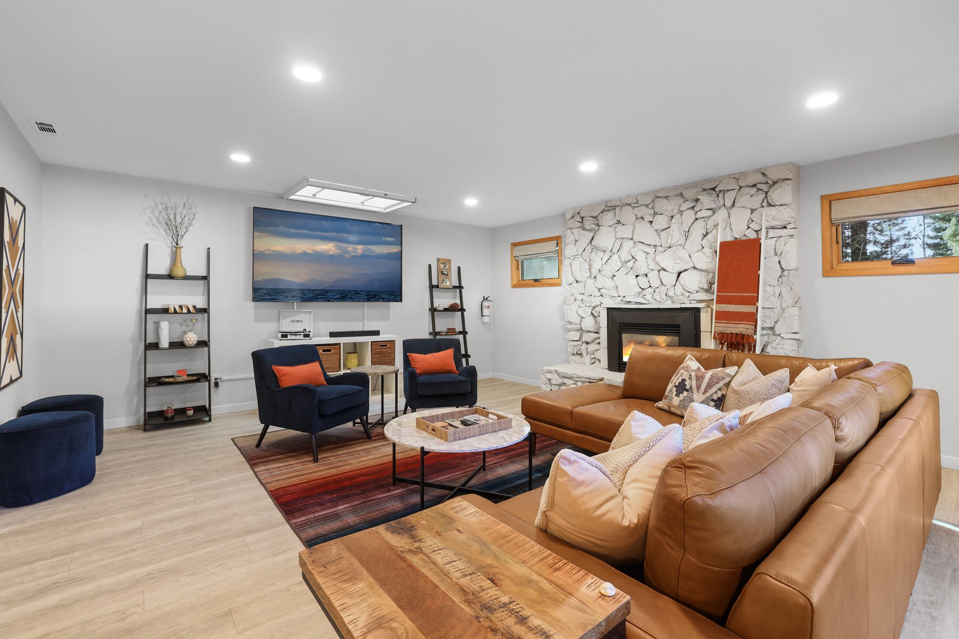 Spacious living room with tan sectional sofa, orange chairs, fireplace, and wall art on light wood floors