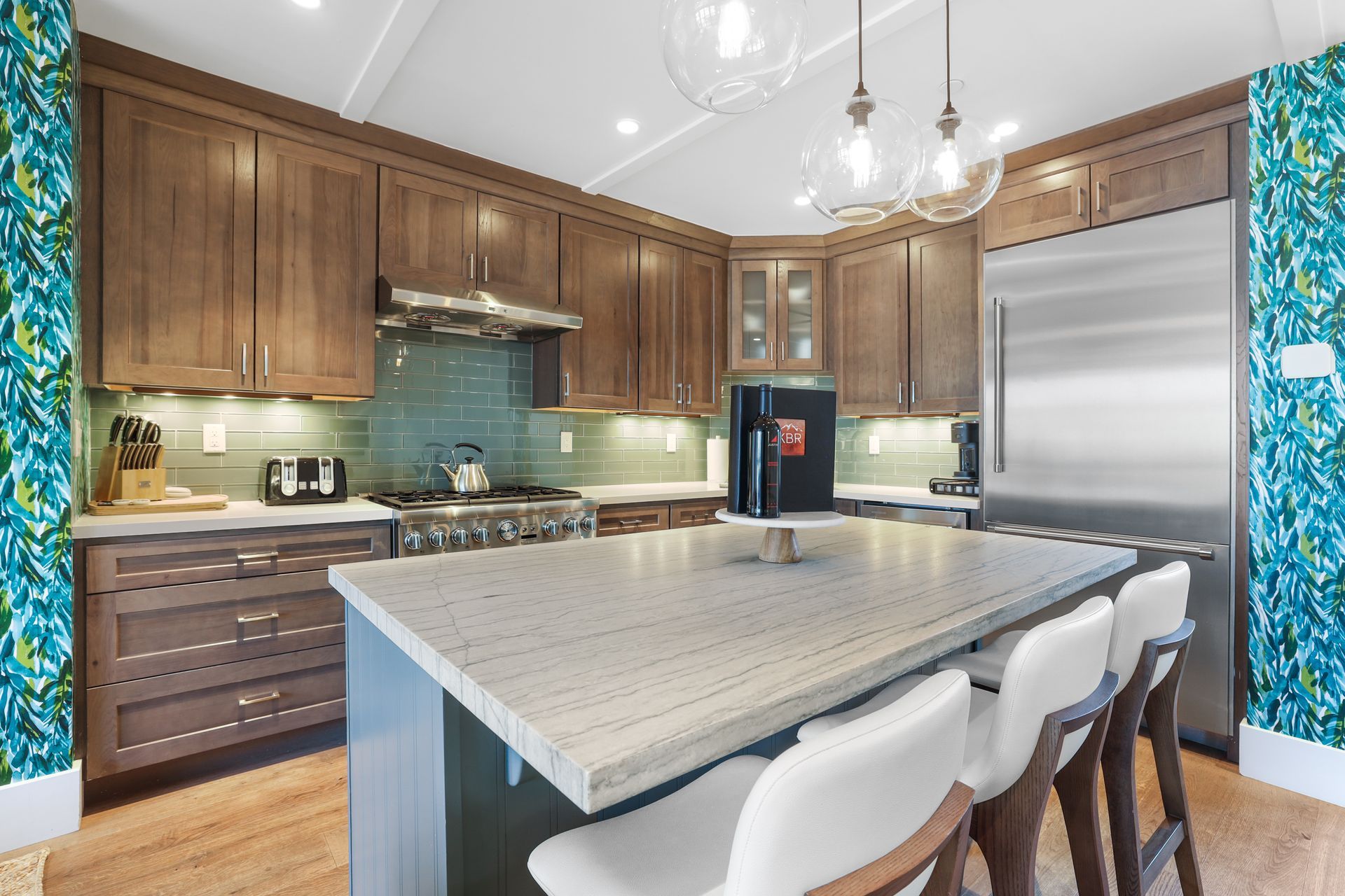 Modern kitchen with wood cabinets, marble island, white barstools, and pendant lights