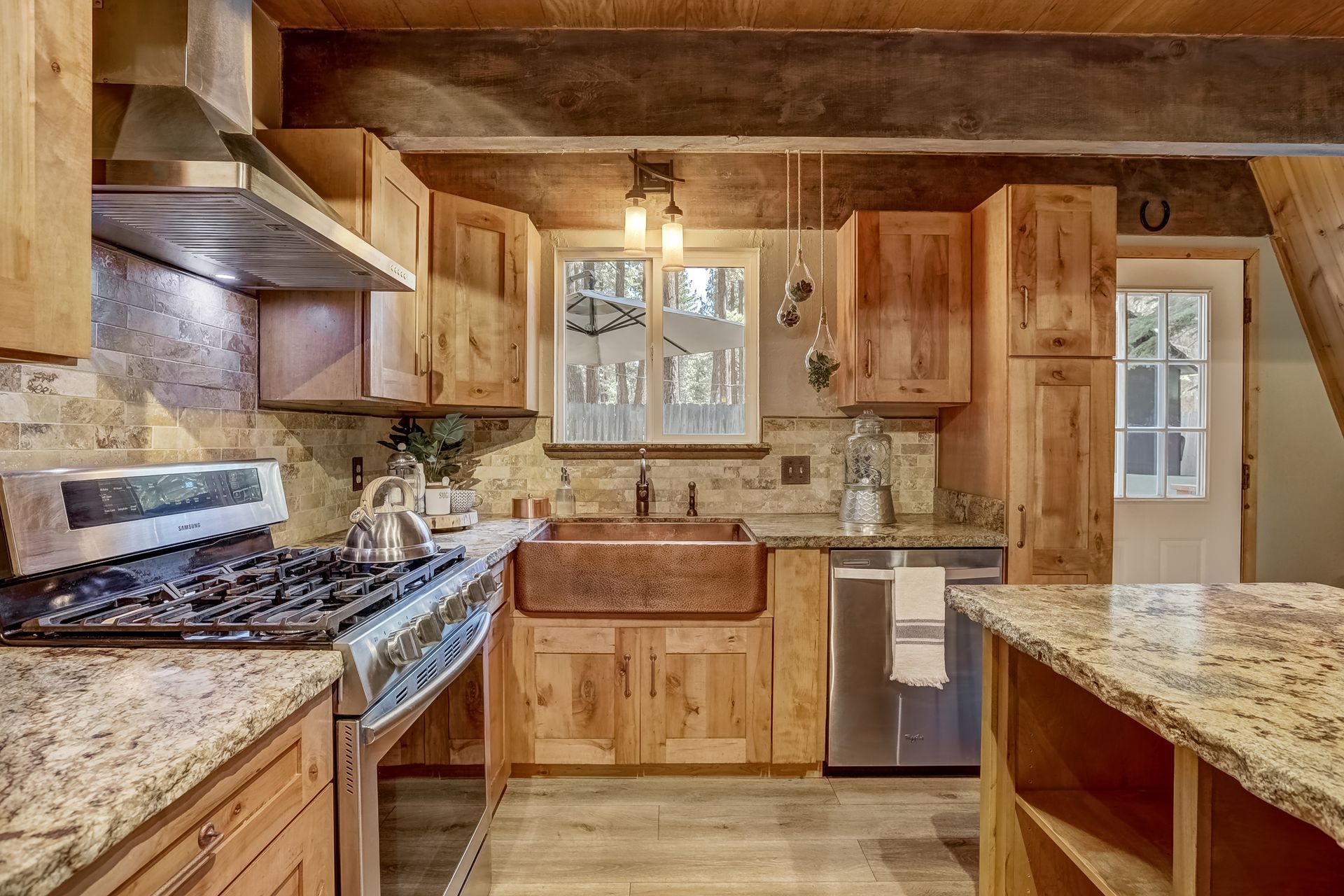 Rustic kitchen with wood cabinets, granite countertops, gas stove, sink under window, and stainless dishwasher