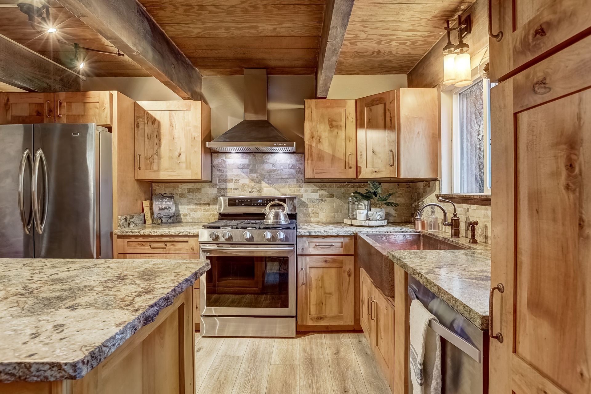 Warm rustic kitchen with wood cabinets, granite counters, stainless-steel appliances, and wood-paneled ceiling.