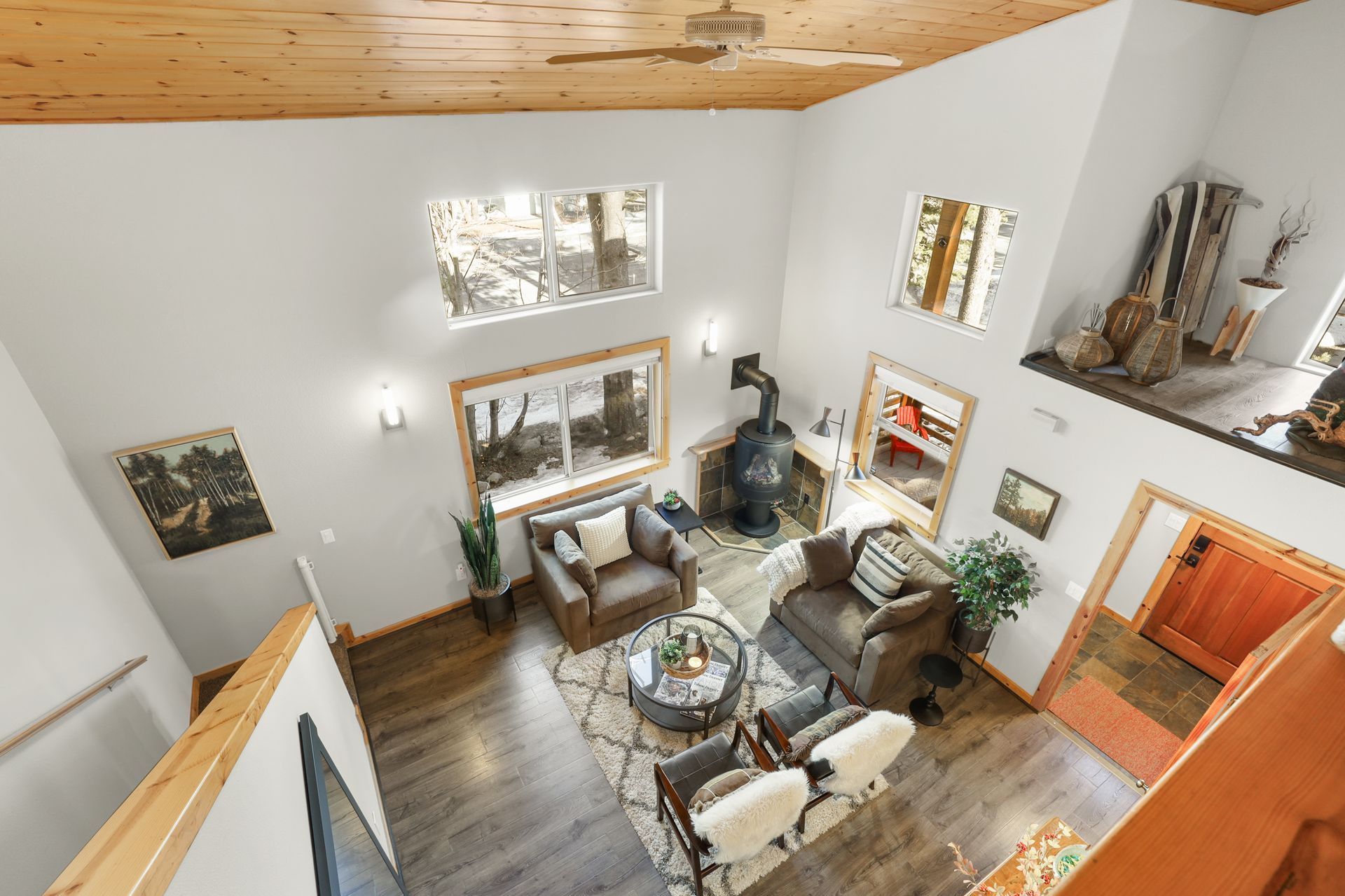 High-ceiling living room with white walls, wood floor, gray sofas, armchairs, and large windows.
