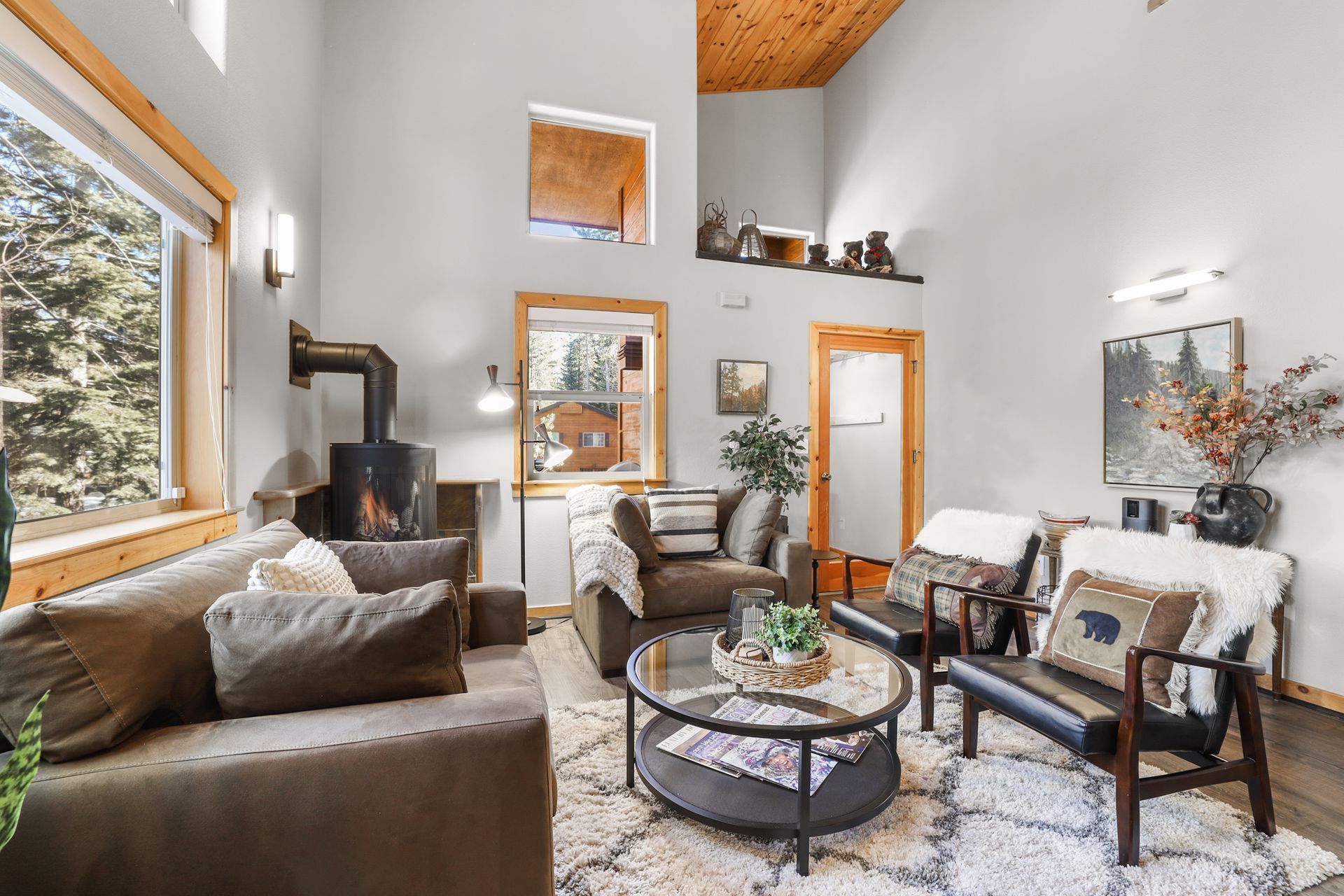 Cozy living room with gray sofa, white chairs, round coffee table, large windows, and fireplace.