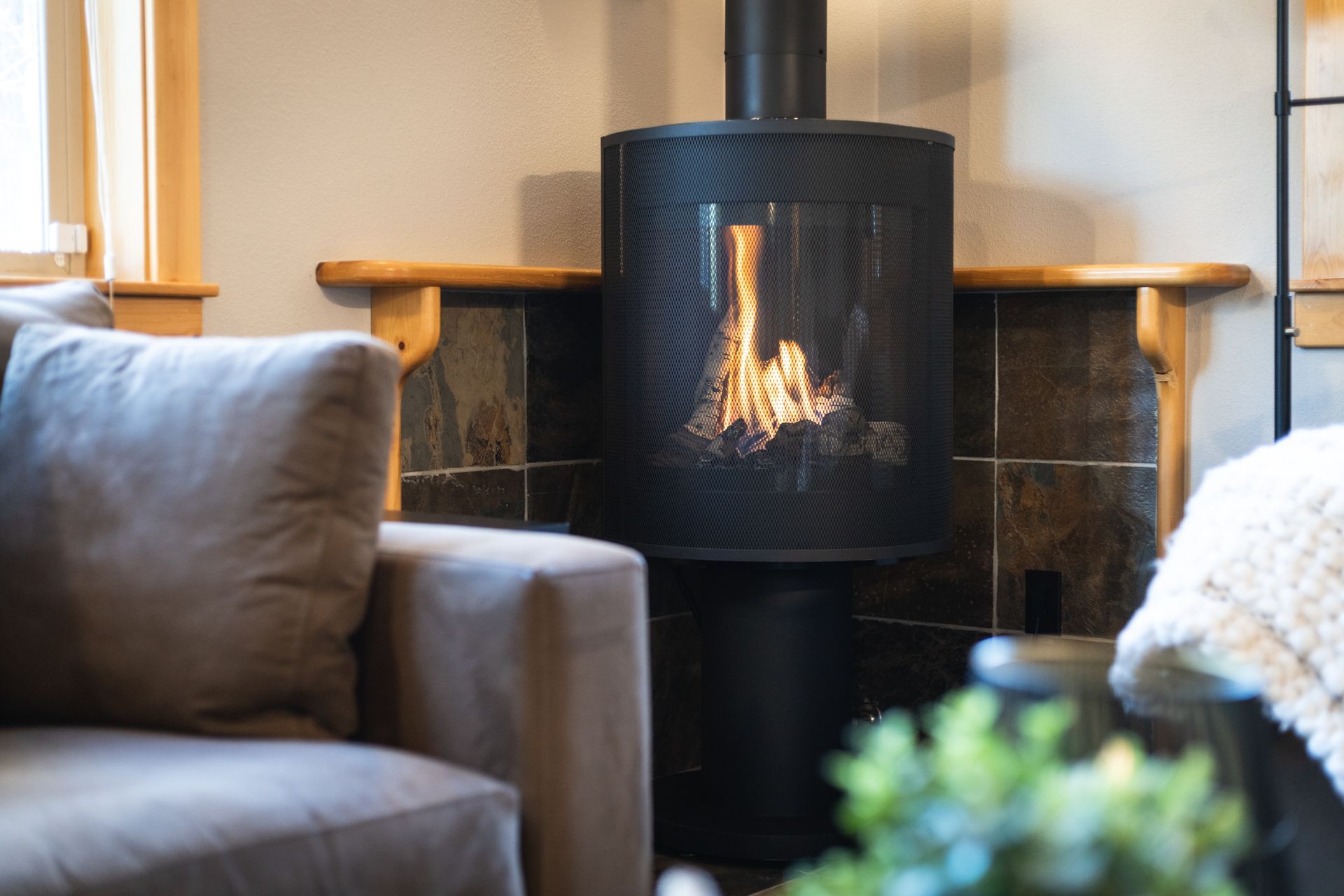 Modern living room with a black wood stove burning beside a gray sofa and a soft blanket