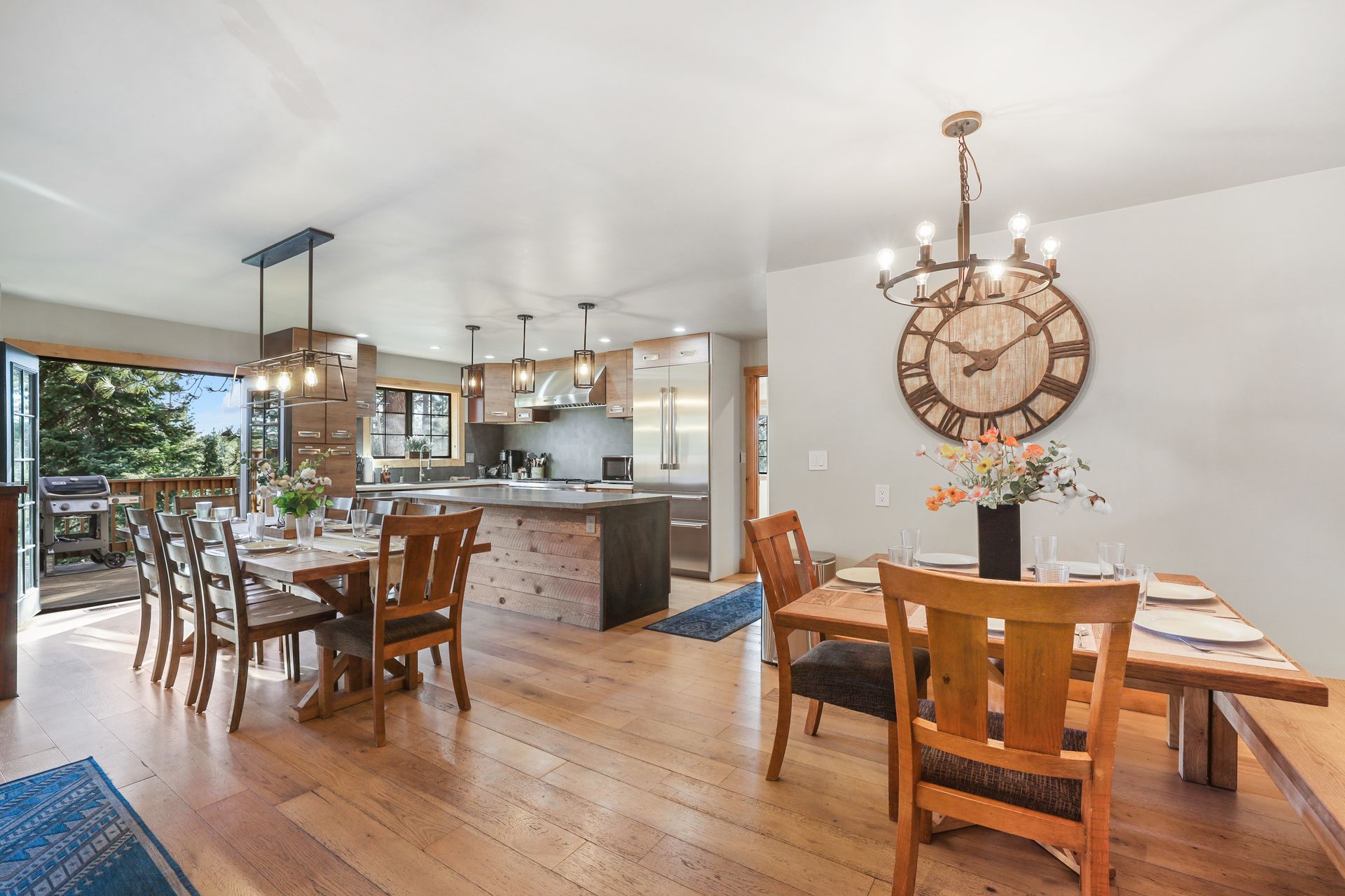 Open-plan dining and kitchen area with wood floors, rustic table, and large wall clock