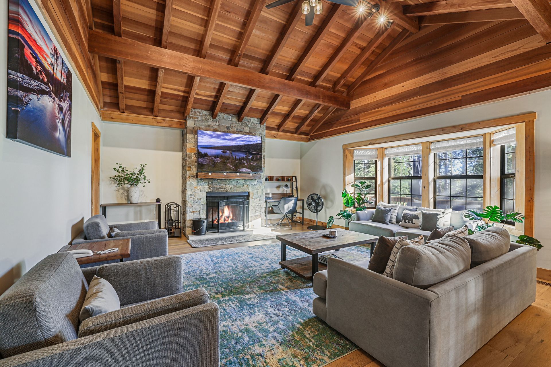 Spacious living room with wood-beamed ceiling, fireplace, sectional sofas, and large windows overlooking outdoors