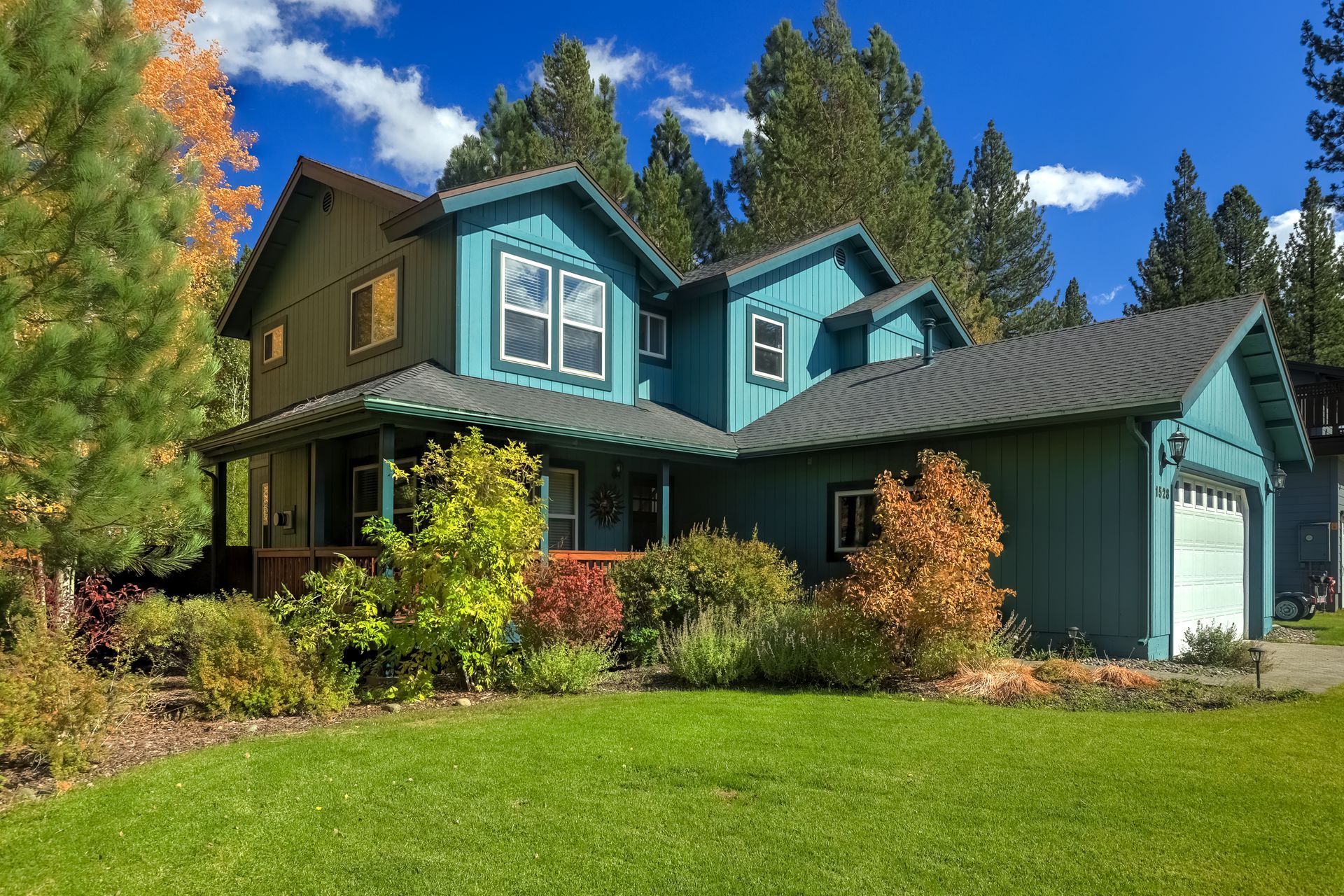 Teal two-story house with garage, green lawn, autumn trees, and blue sky