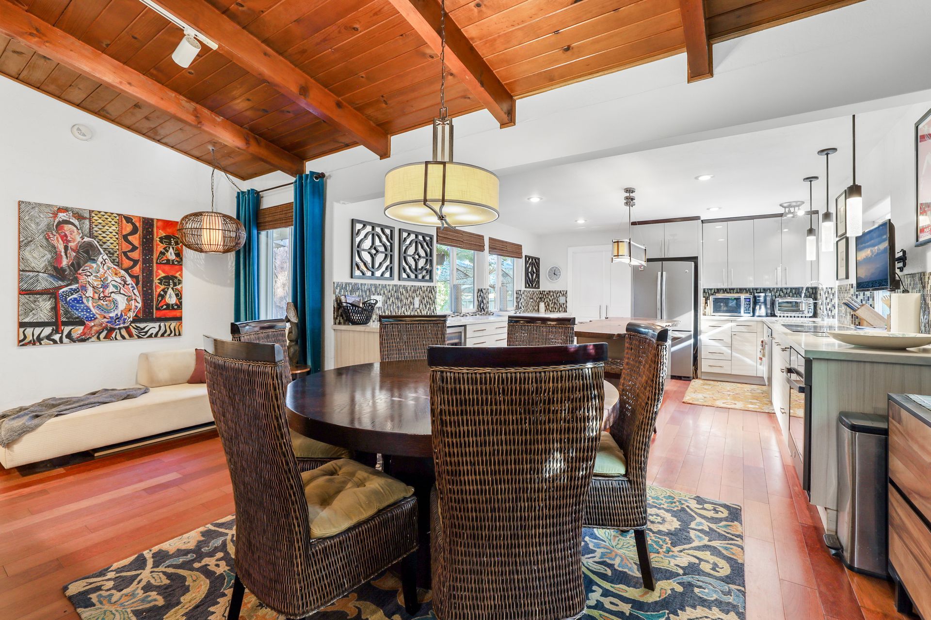 Open-plan living and dining area with wood ceiling, wicker chairs, and a kitchen in the background