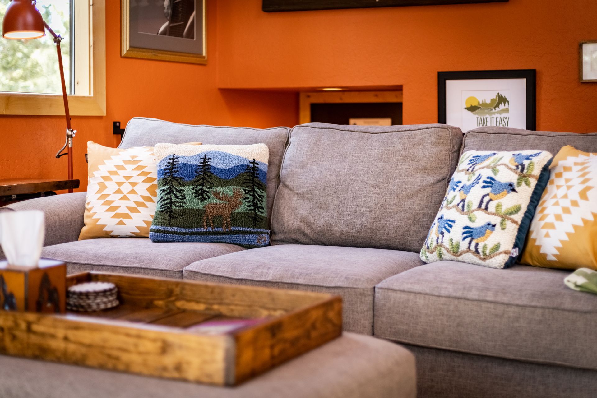 Orange-walled living room with beige sofa, patterned pillows, and a wooden tray table