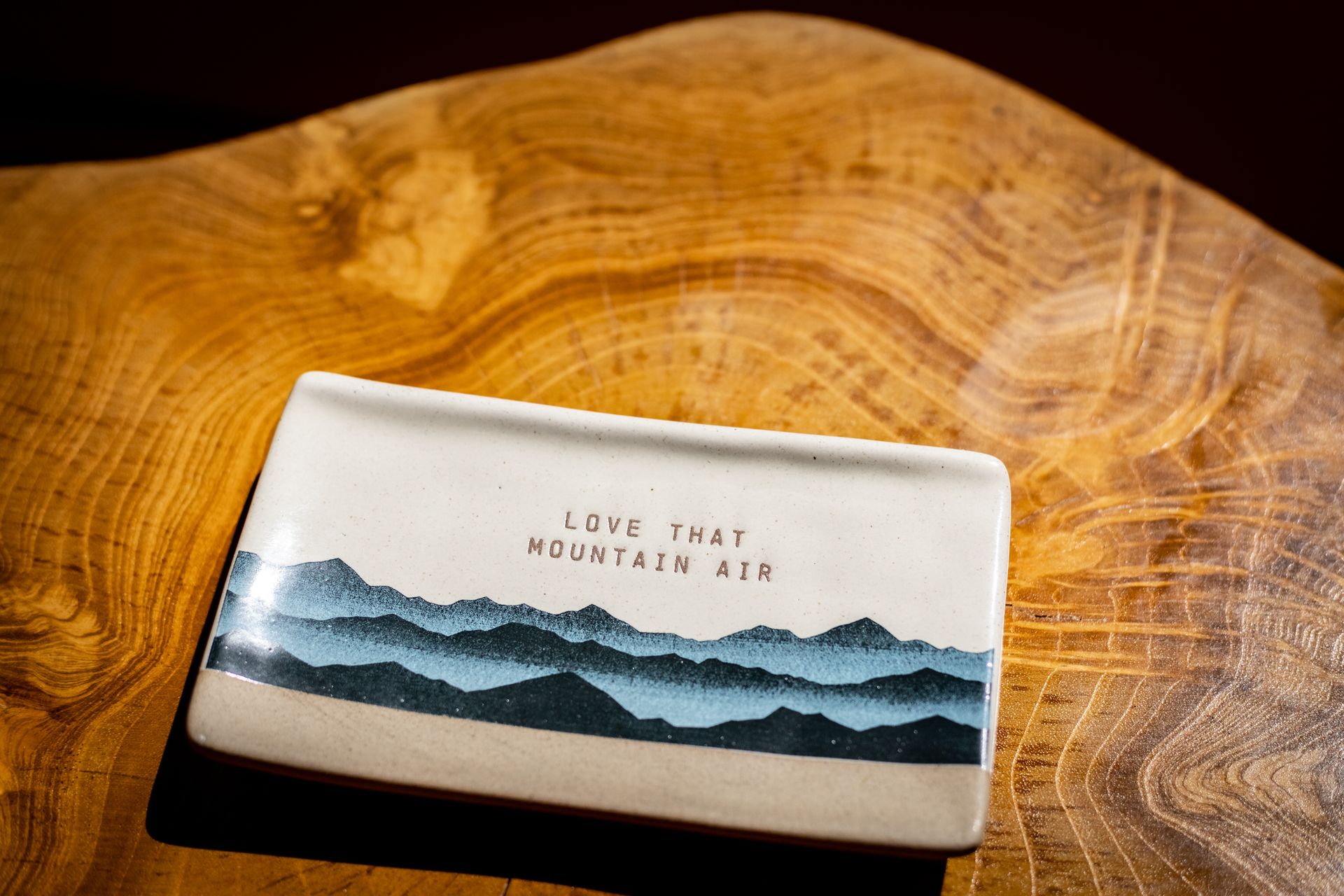 Ceramic tray with blue mountain scene and small text on a wooden surface