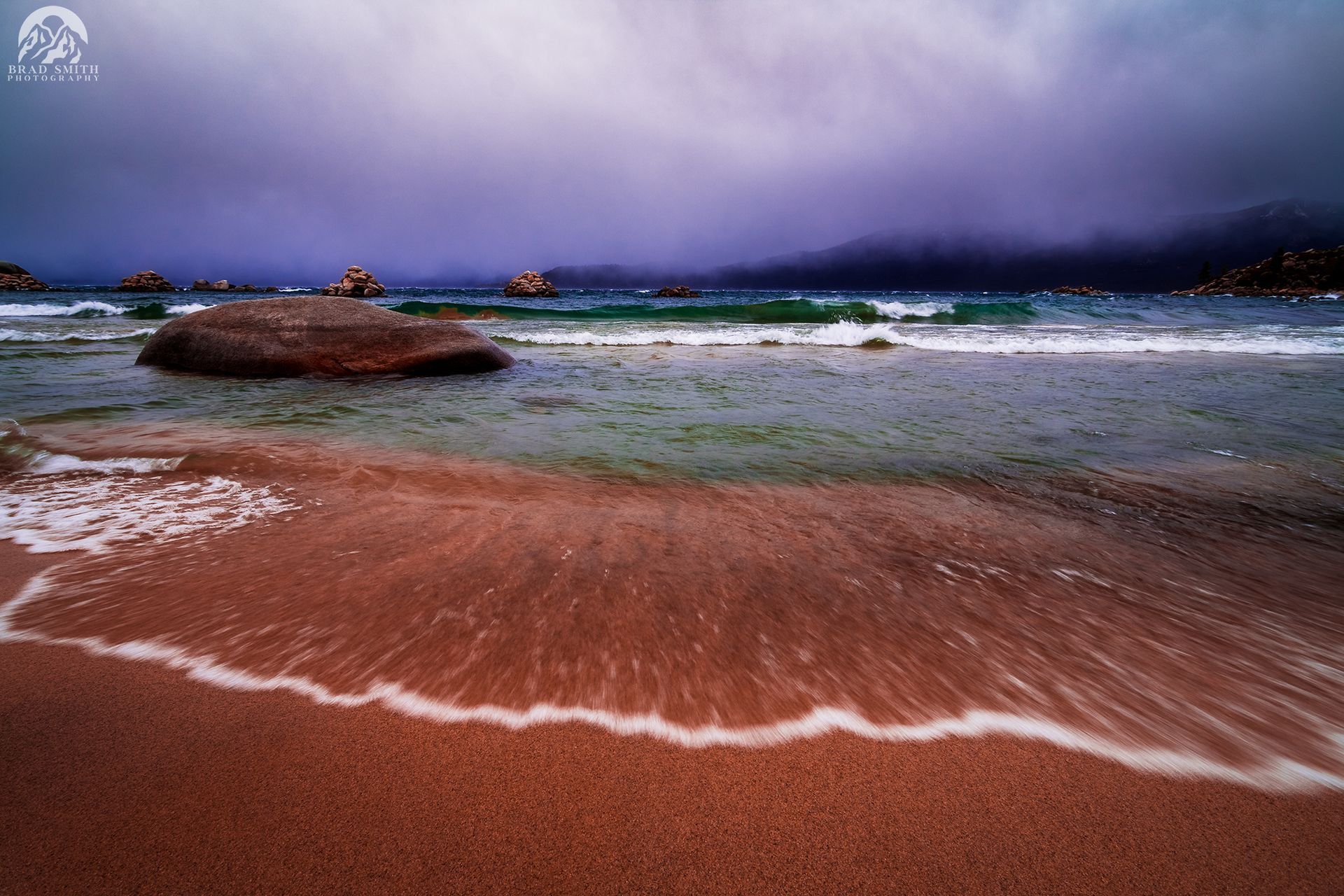 Stormy beach with crashing waves, reddish sand, and dark clouds over the horizon