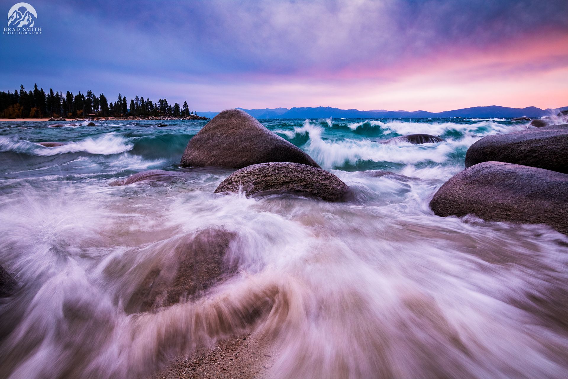 Rocky shoreline with waves rushing under a purple-pink dusk sky