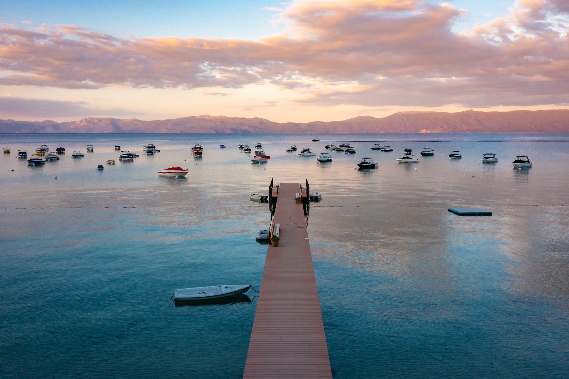 Wooden pier stretching into a calm blue bay at sunset, with many small boats anchored nearby