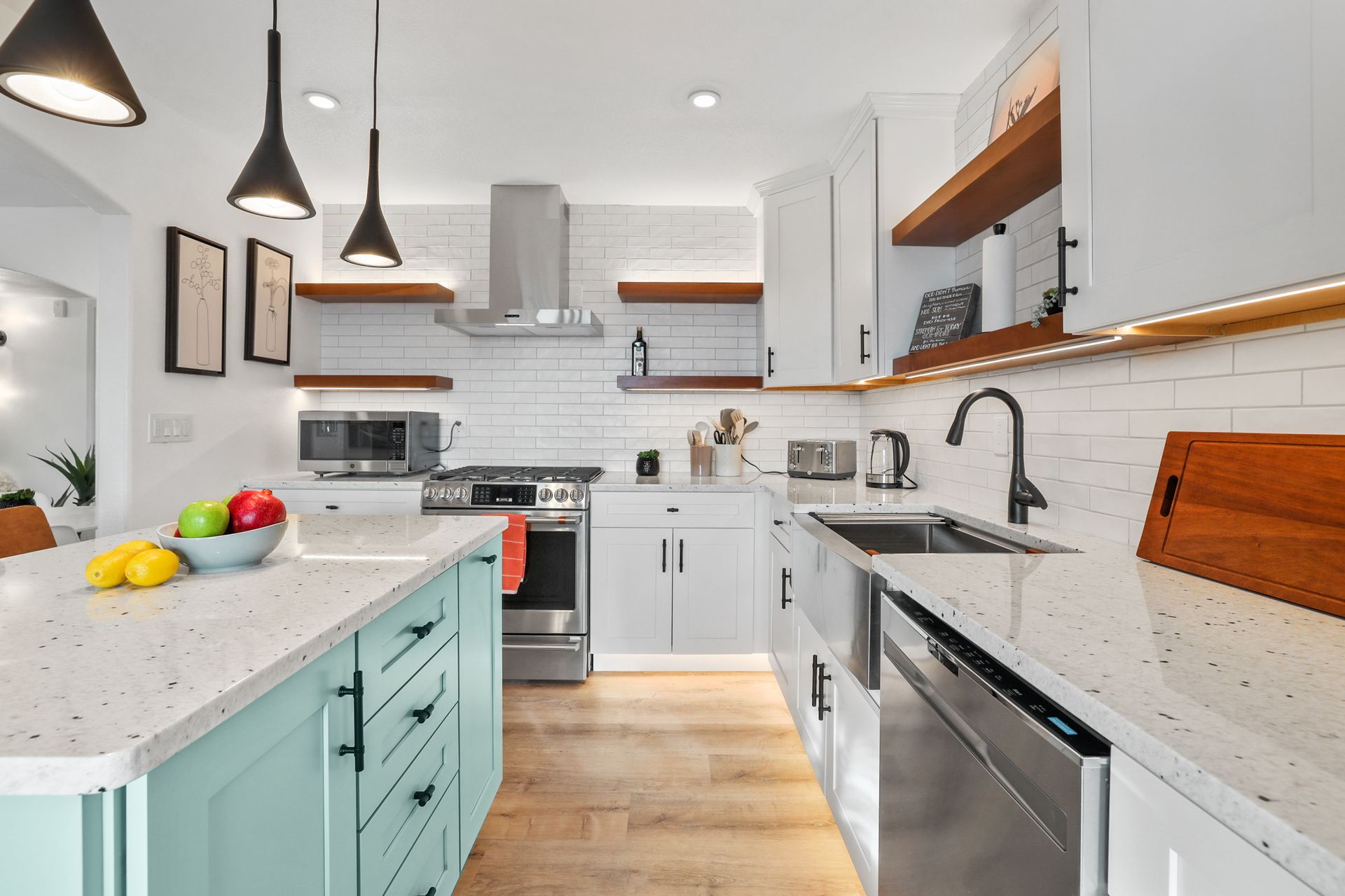 Bright modern kitchen with white cabinets, marble counters, teal island, and wood floors