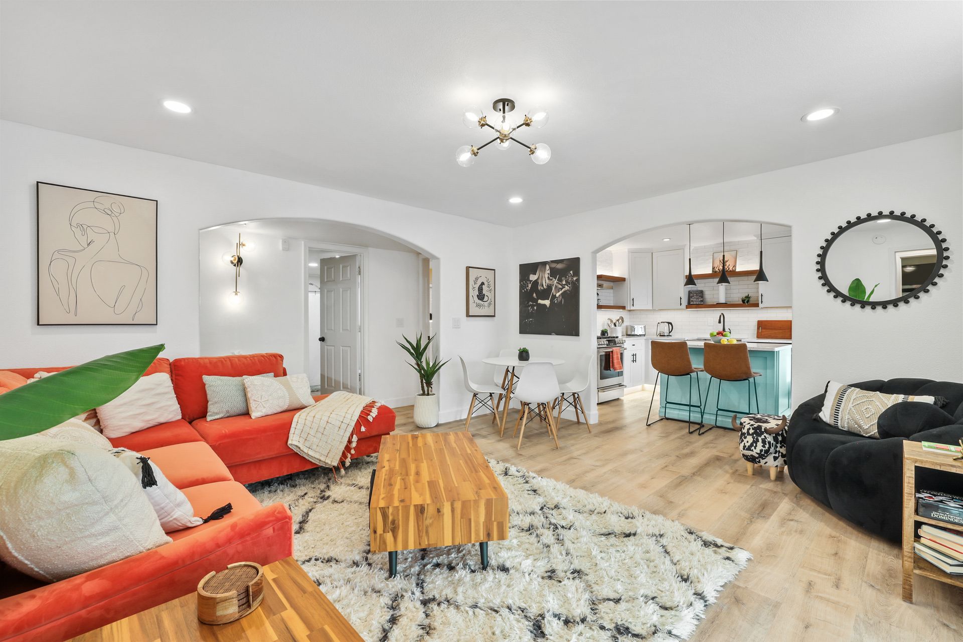 Bright living room with red sectional, patterned rug, wood coffee table, and open dining area with turquoise chairs