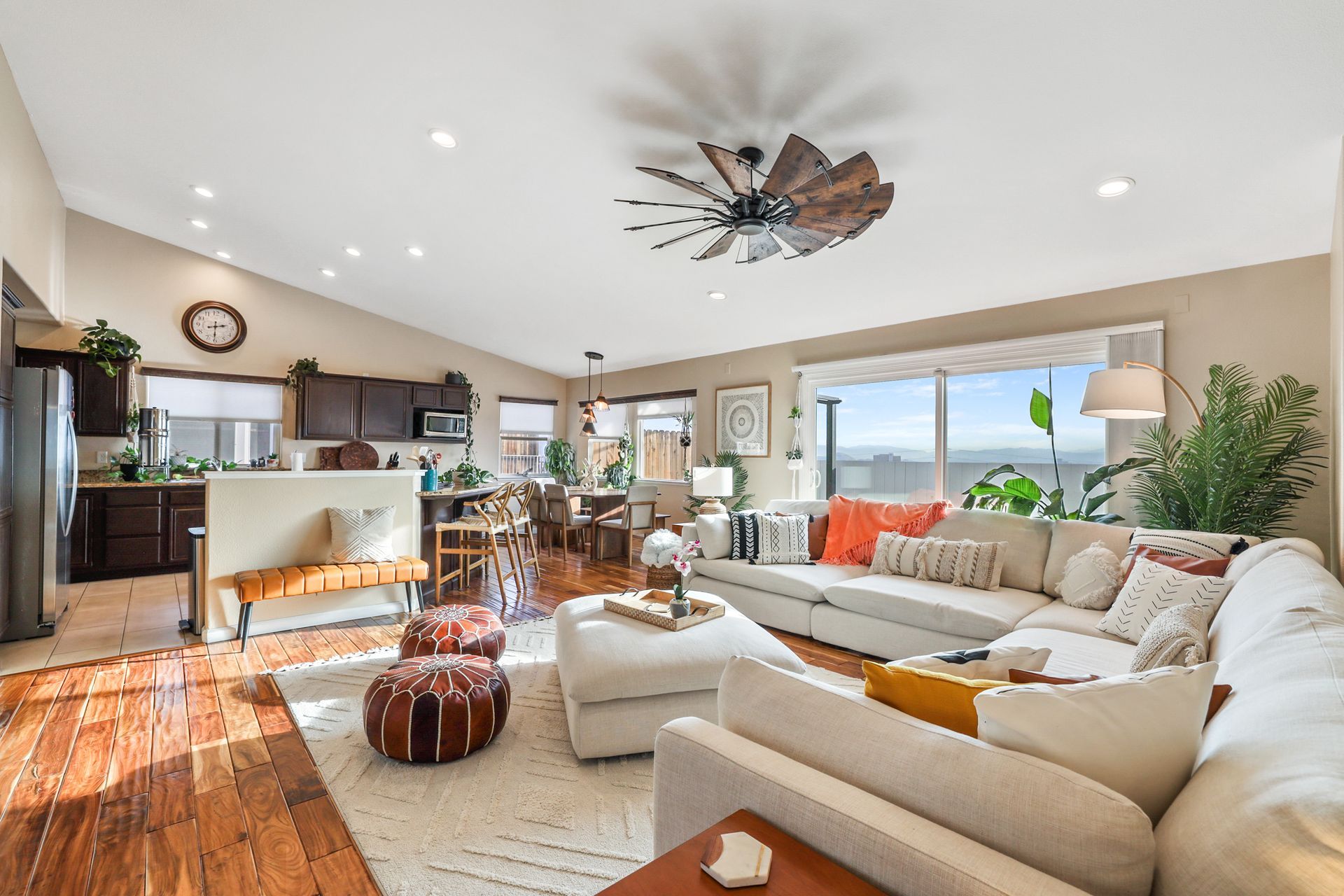 Bright open-plan living room with cream sofas, wood floors, kitchen bar, and large windows overlooking a view