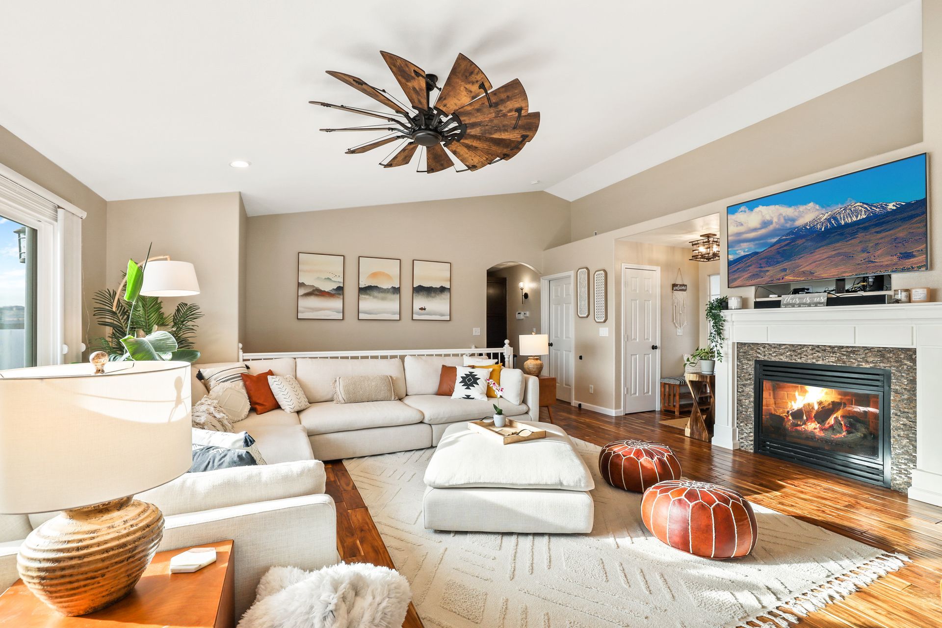 Bright living room with white sectional, fireplace, large windows, and ceiling fan; ocean view artwork.