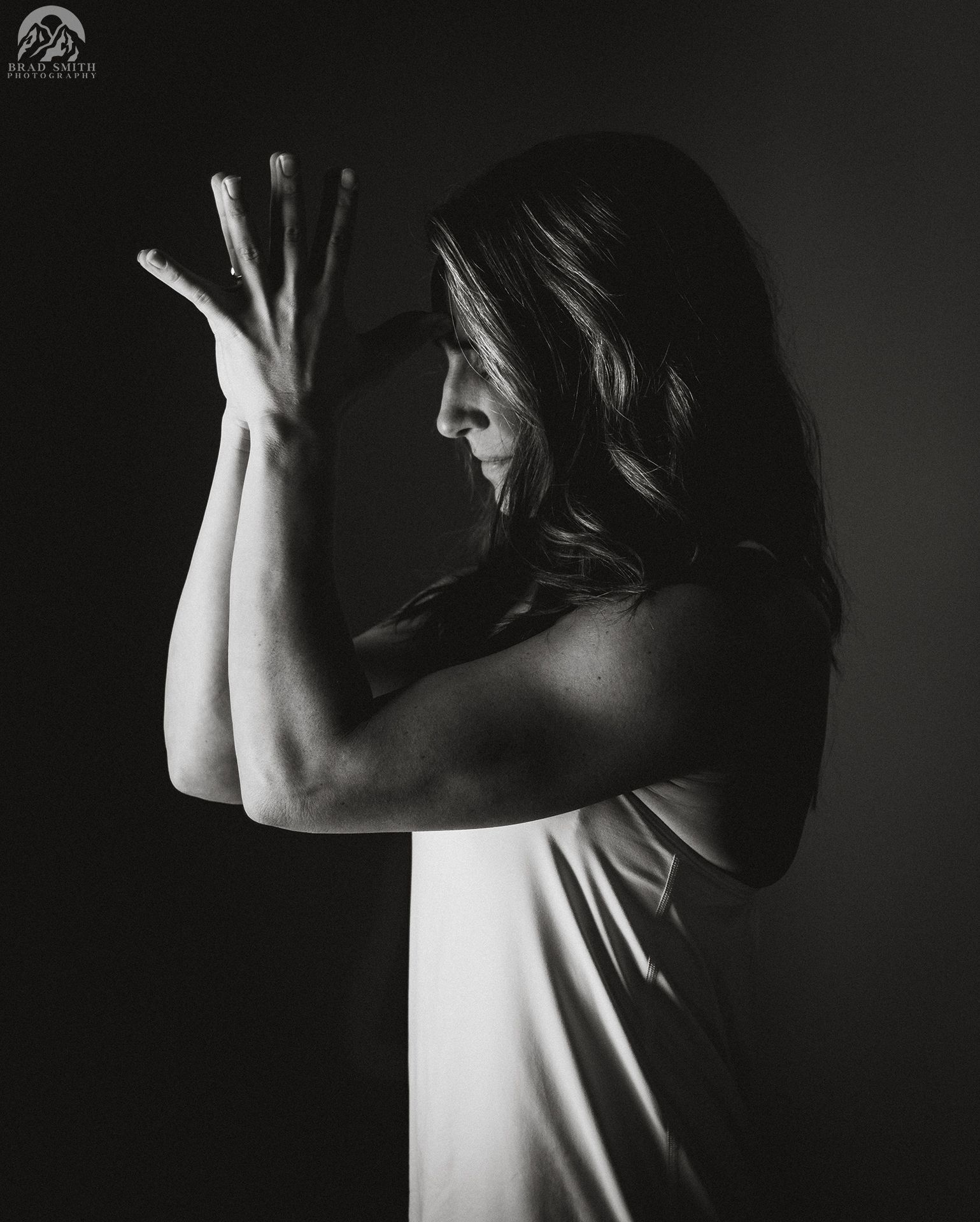 Black-and-white profile of a woman posing with raised hands against a dark background
