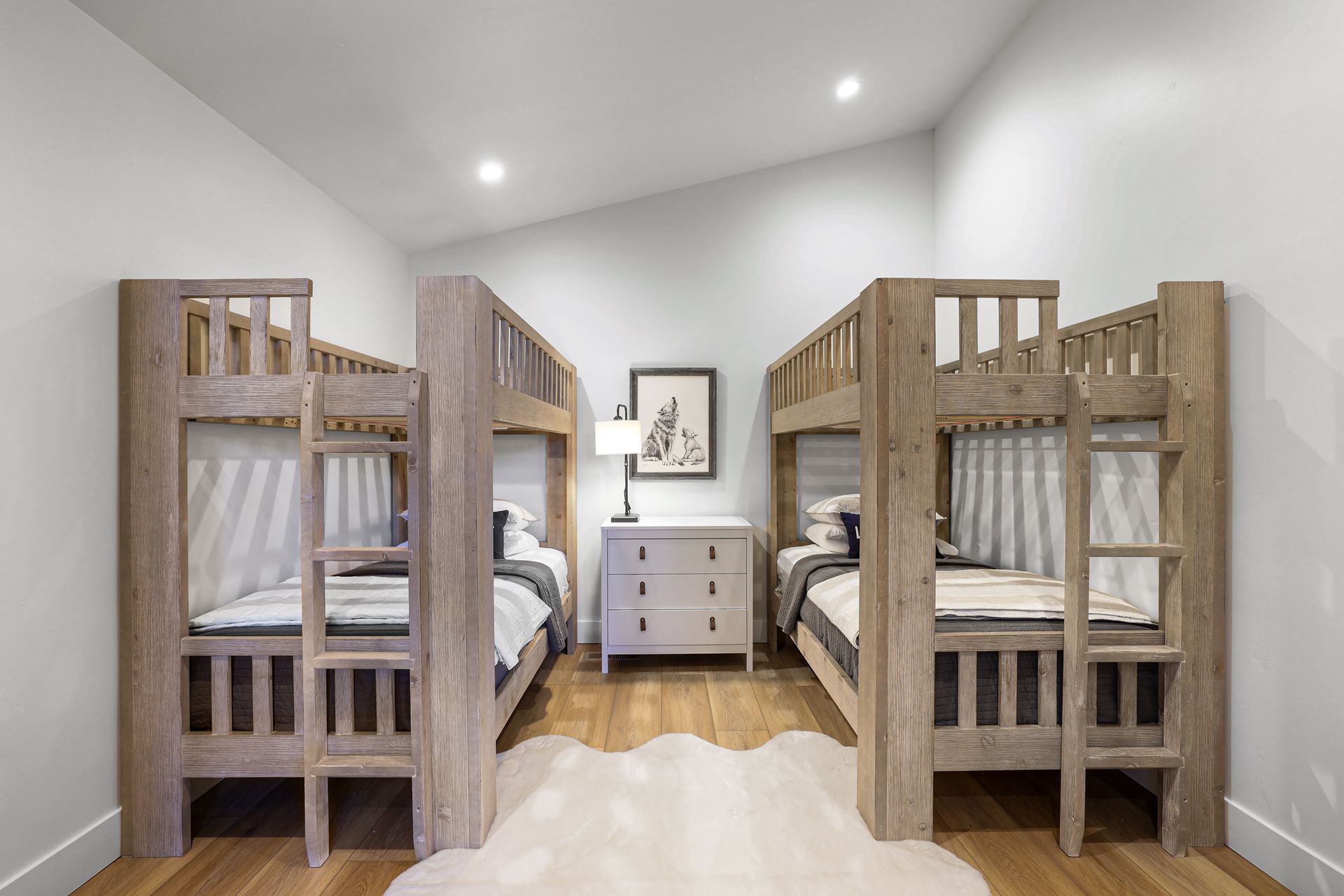 Bright bedroom with two wooden bunk beds, a white dresser, and a rug on a hardwood floor.
