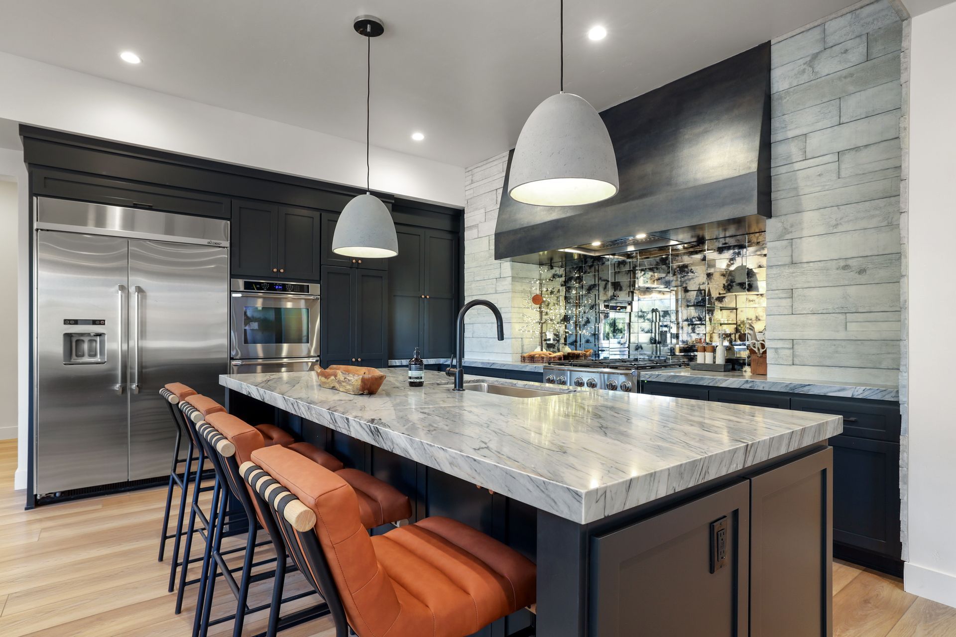 Modern kitchen with marble island, orange stools, pendant lights, and stainless steel appliances