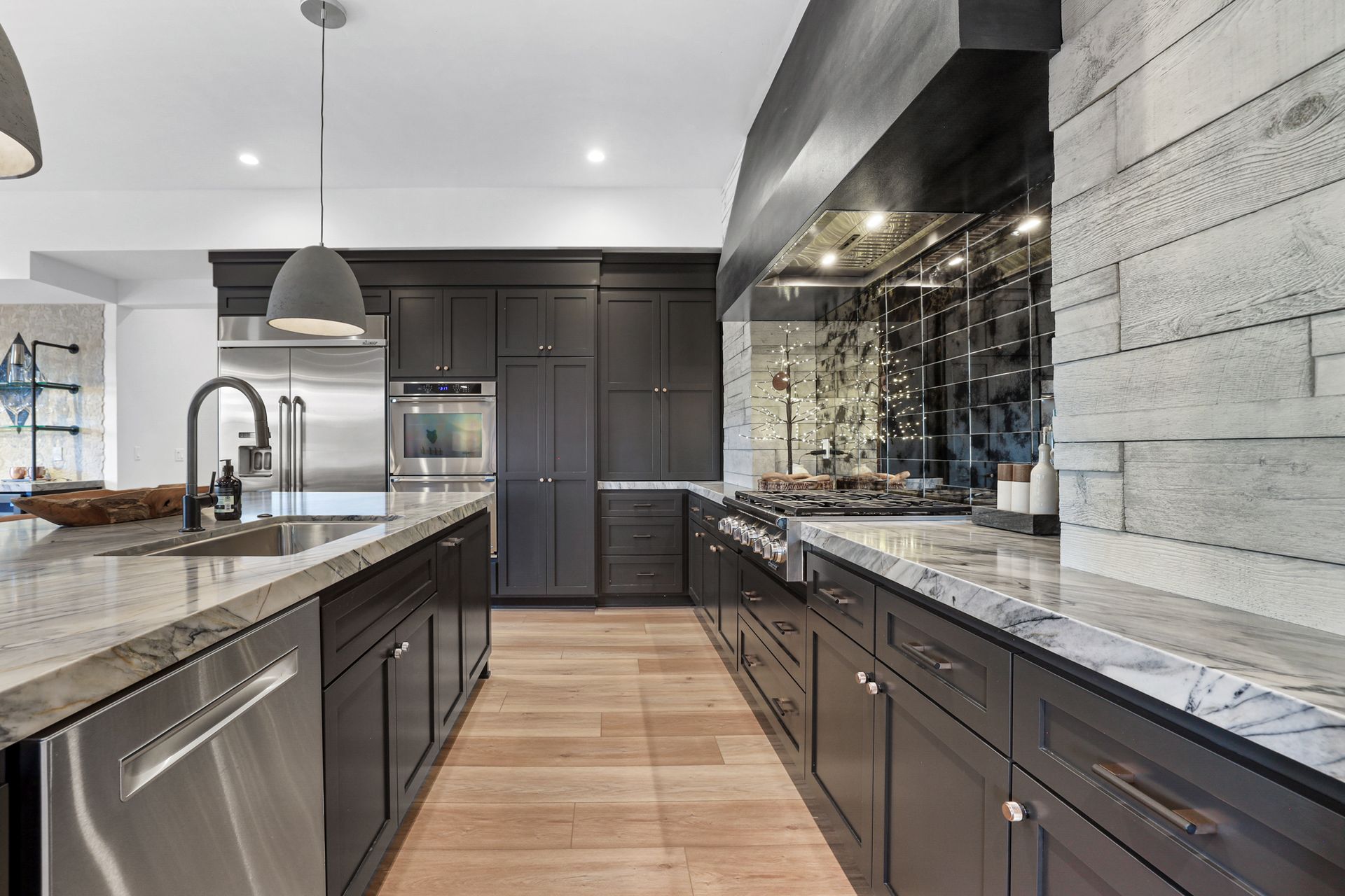 Modern kitchen with dark cabinets, marble countertops, stainless appliances, and a large island