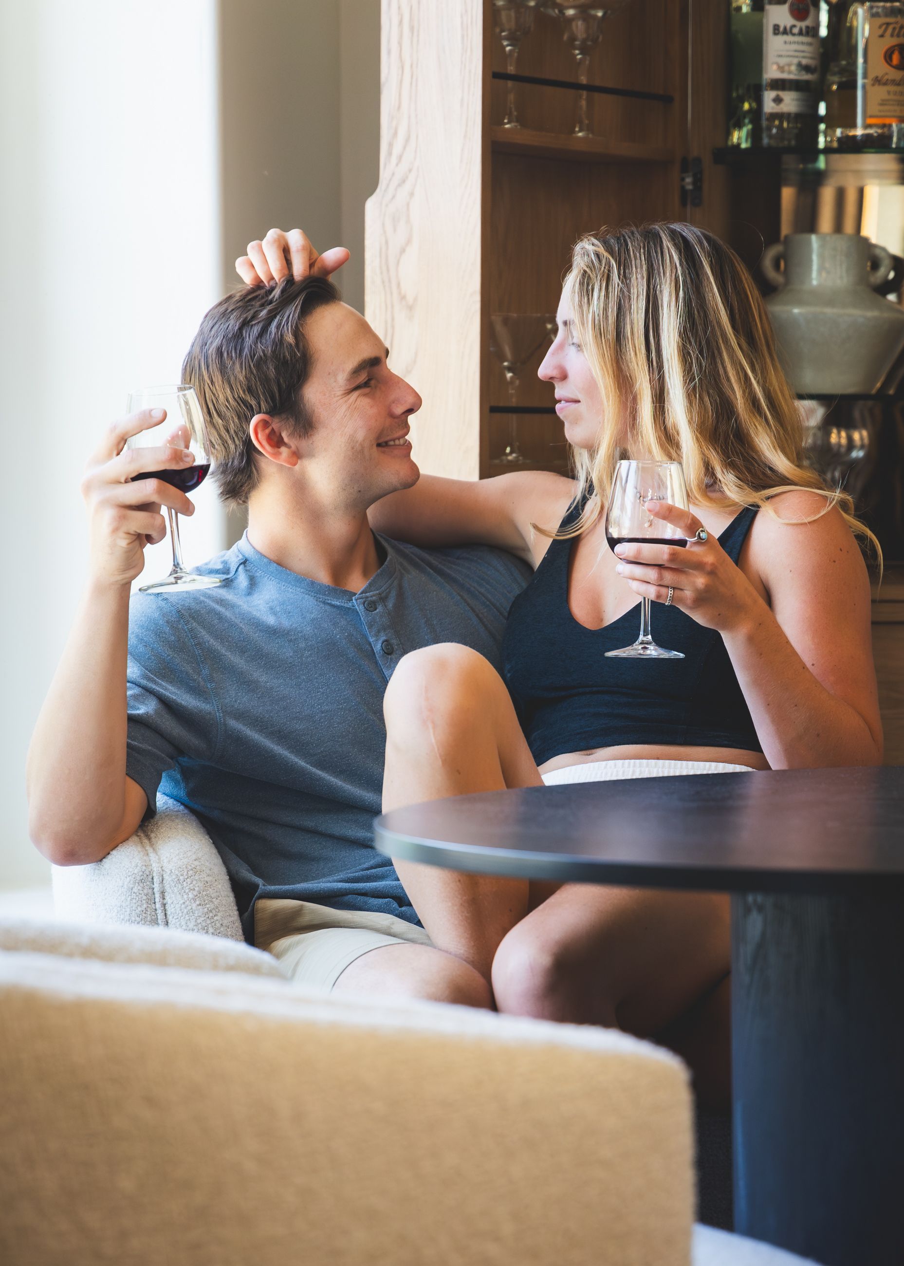 Couple smiling on a couch, holding wine glasses and chatting in a cozy lounge