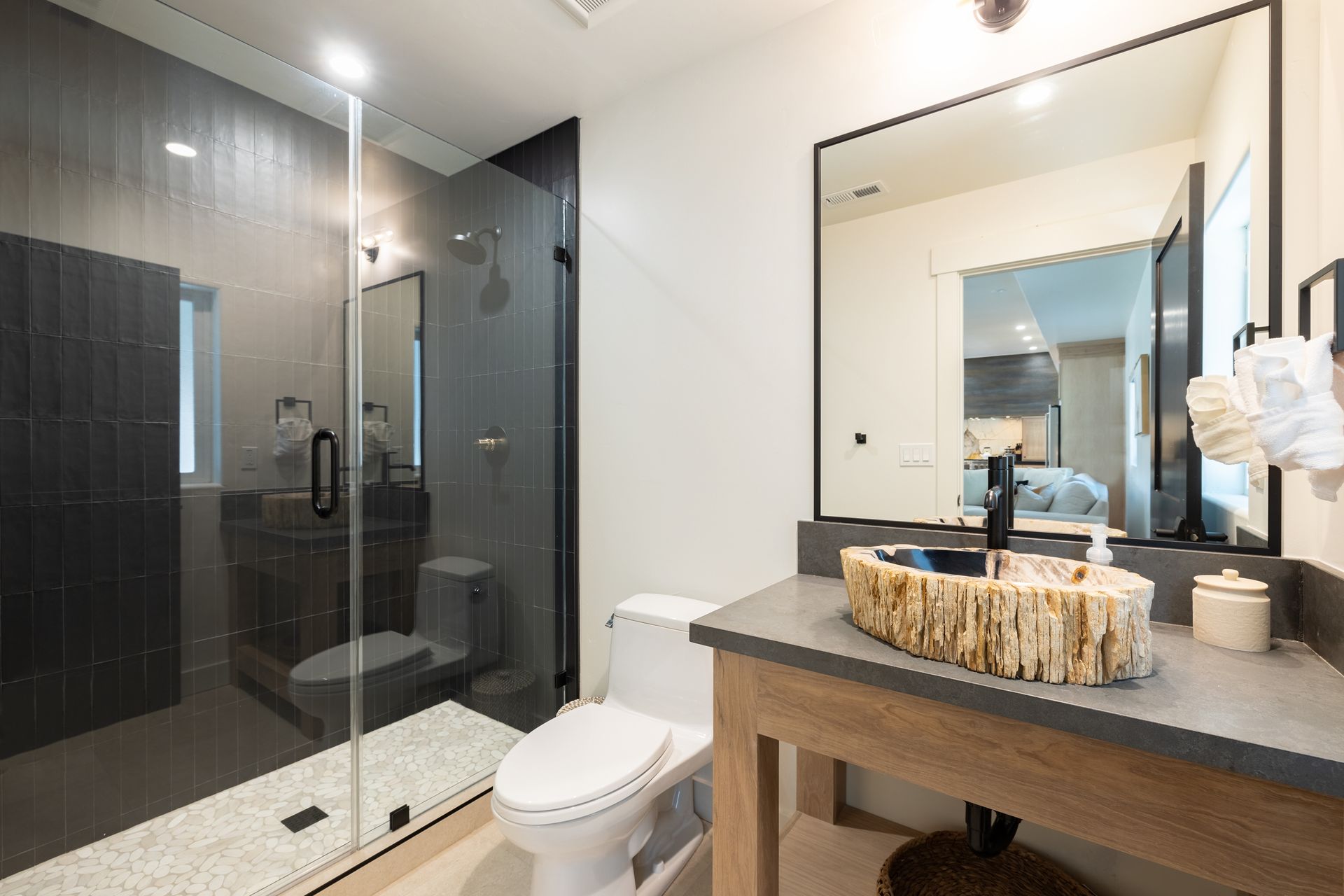 Modern bathroom with glass shower, toilet, and wooden vanity with mirror and woven tray