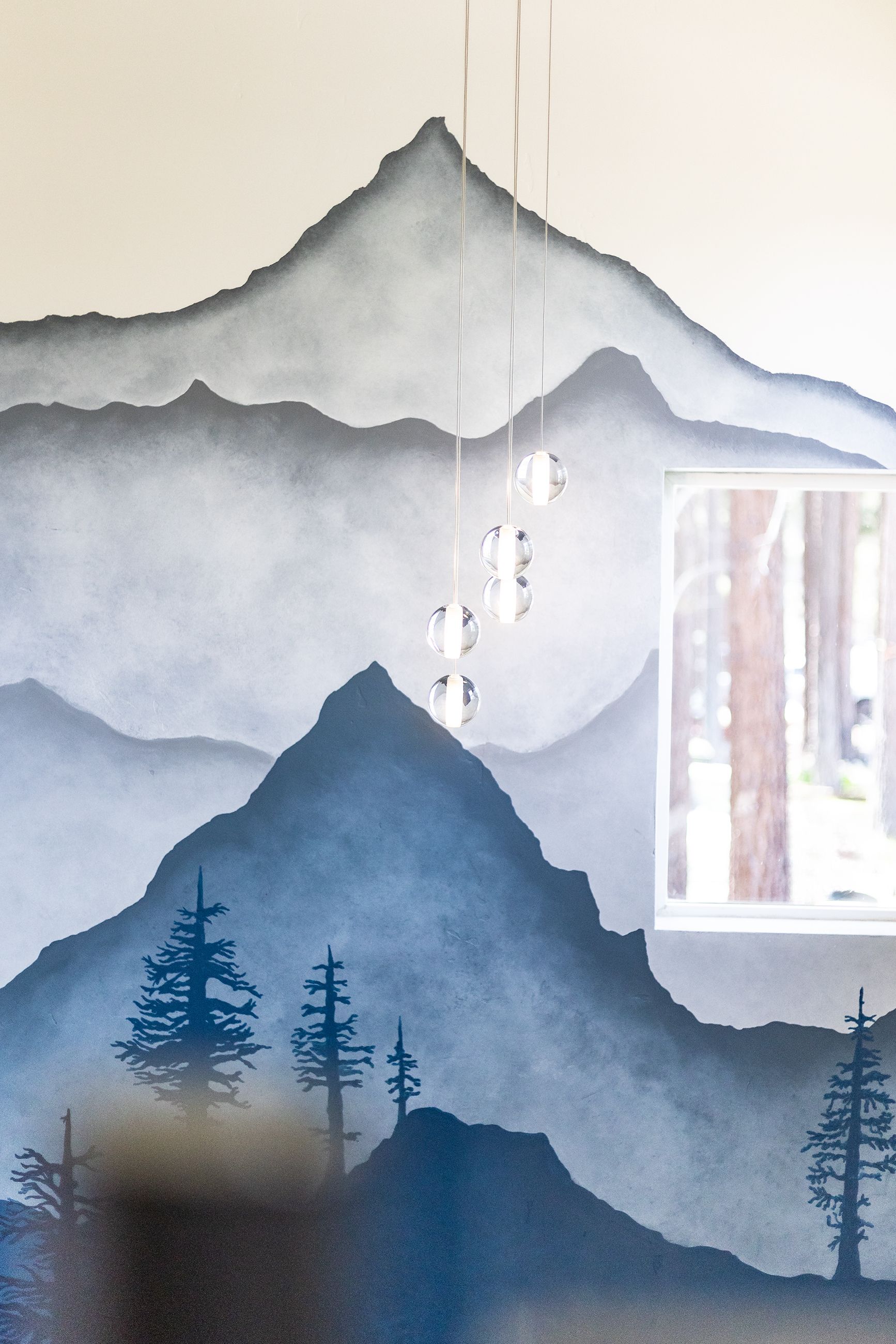 Blue-gray mountain mural with layered peaks, pine silhouettes, and a window on the right.
