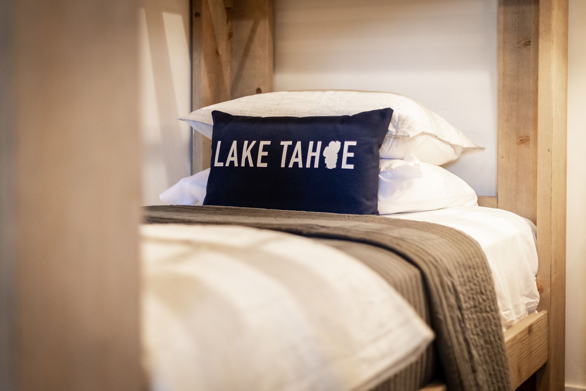 Cozy bed with white linens and a navy “Lake Tahoe” pillow in a wooden room
