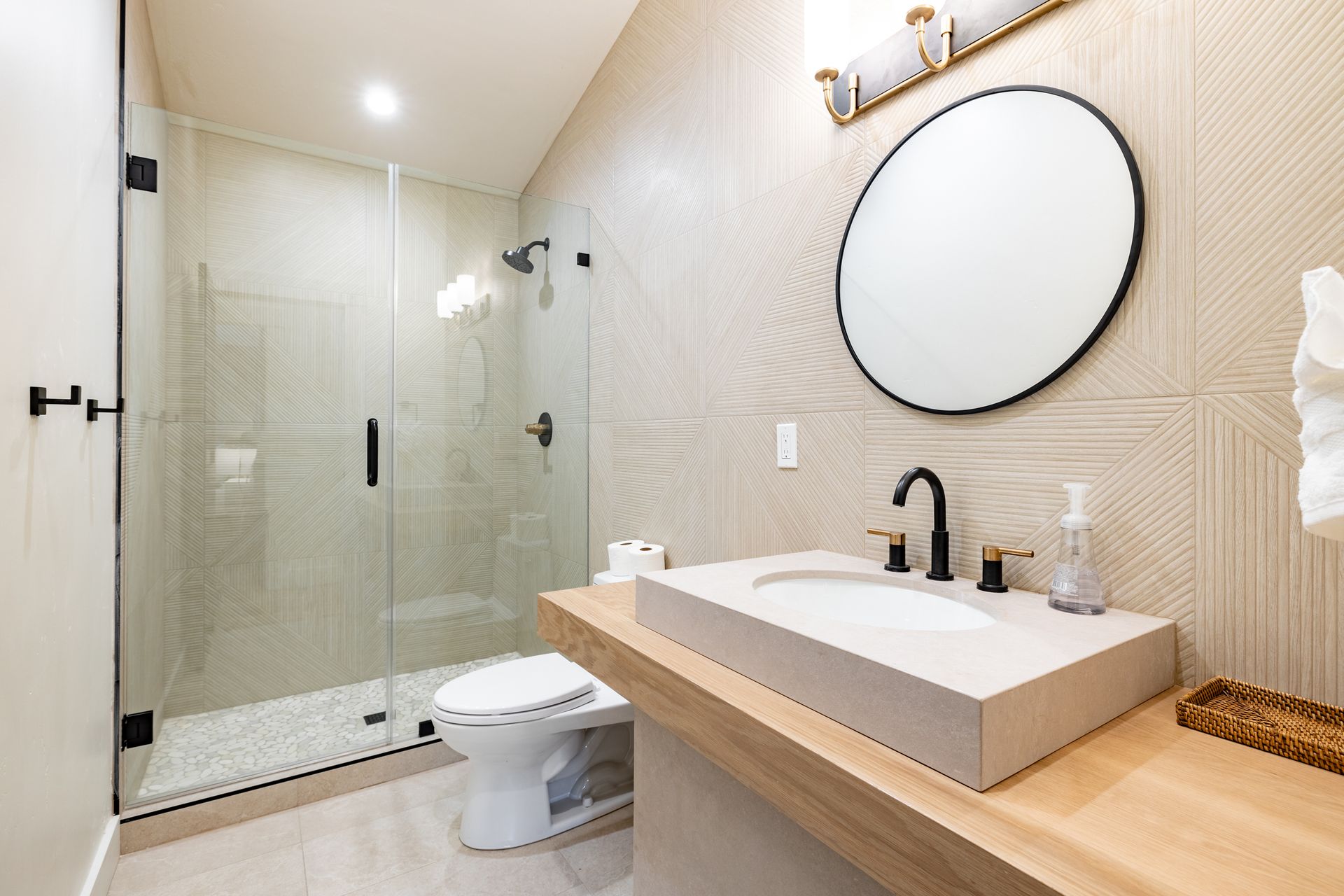 Modern bathroom with glass shower, floating wood vanity, round mirror, and toilet