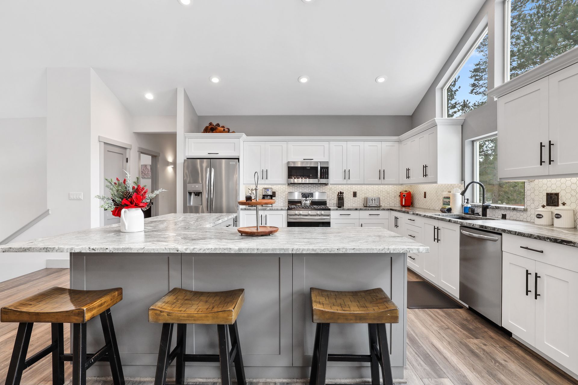 Modern white kitchen with marble island, three stools, and stainless steel appliances