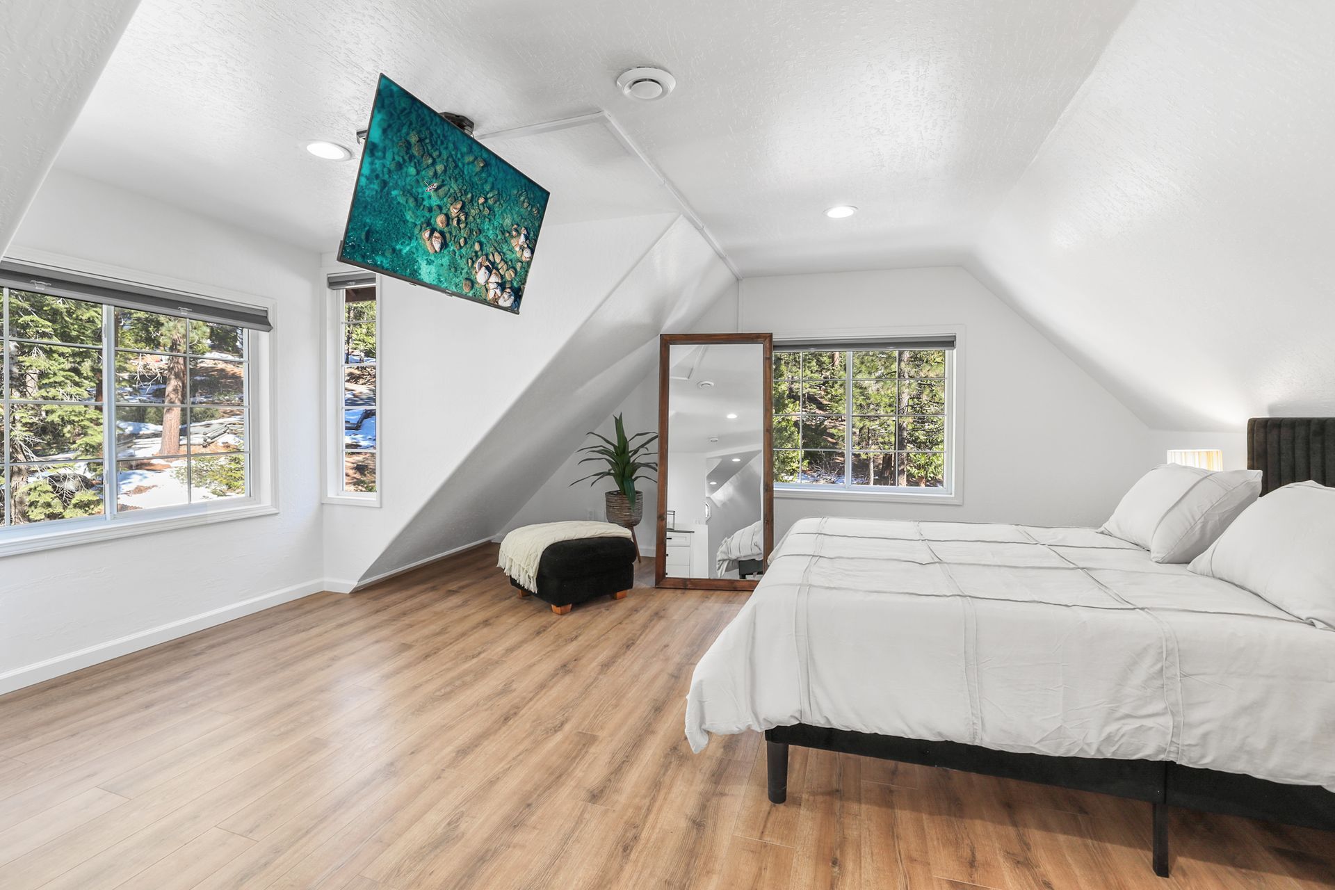 Bright attic bedroom with white walls, wood floors, large windows, and a bed near a slanted ceiling.