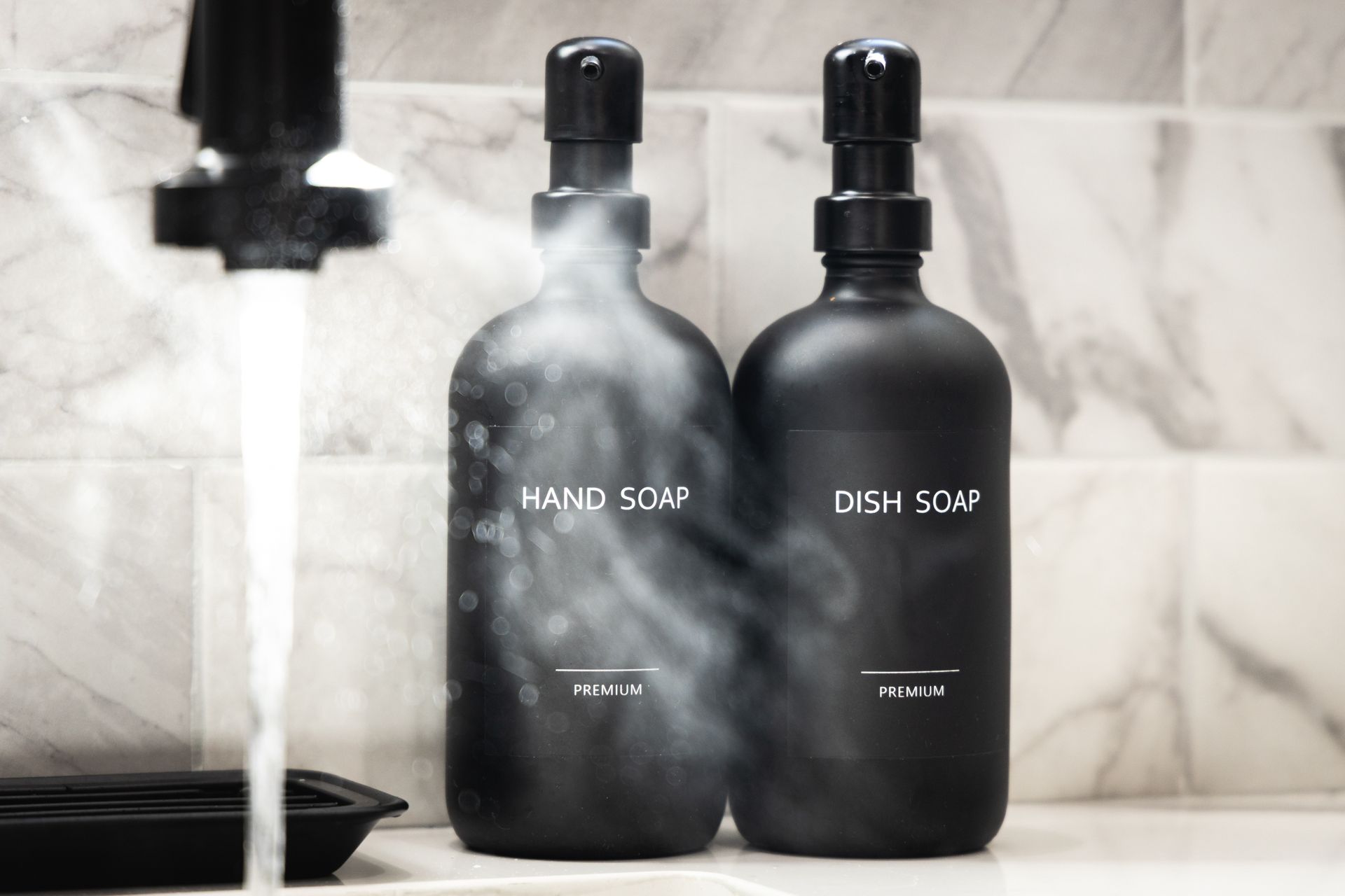 Black bathroom soap dispensers labeled hand soap and dish soap beside a running faucet