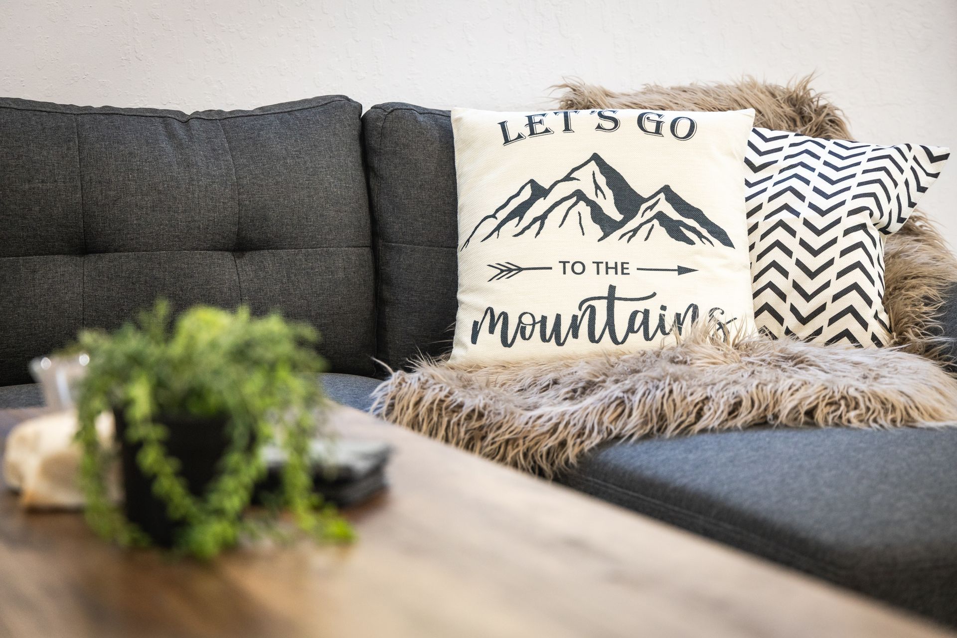 Living room sofa with decorative pillows, including one reading “Let’s go to the mountains.”